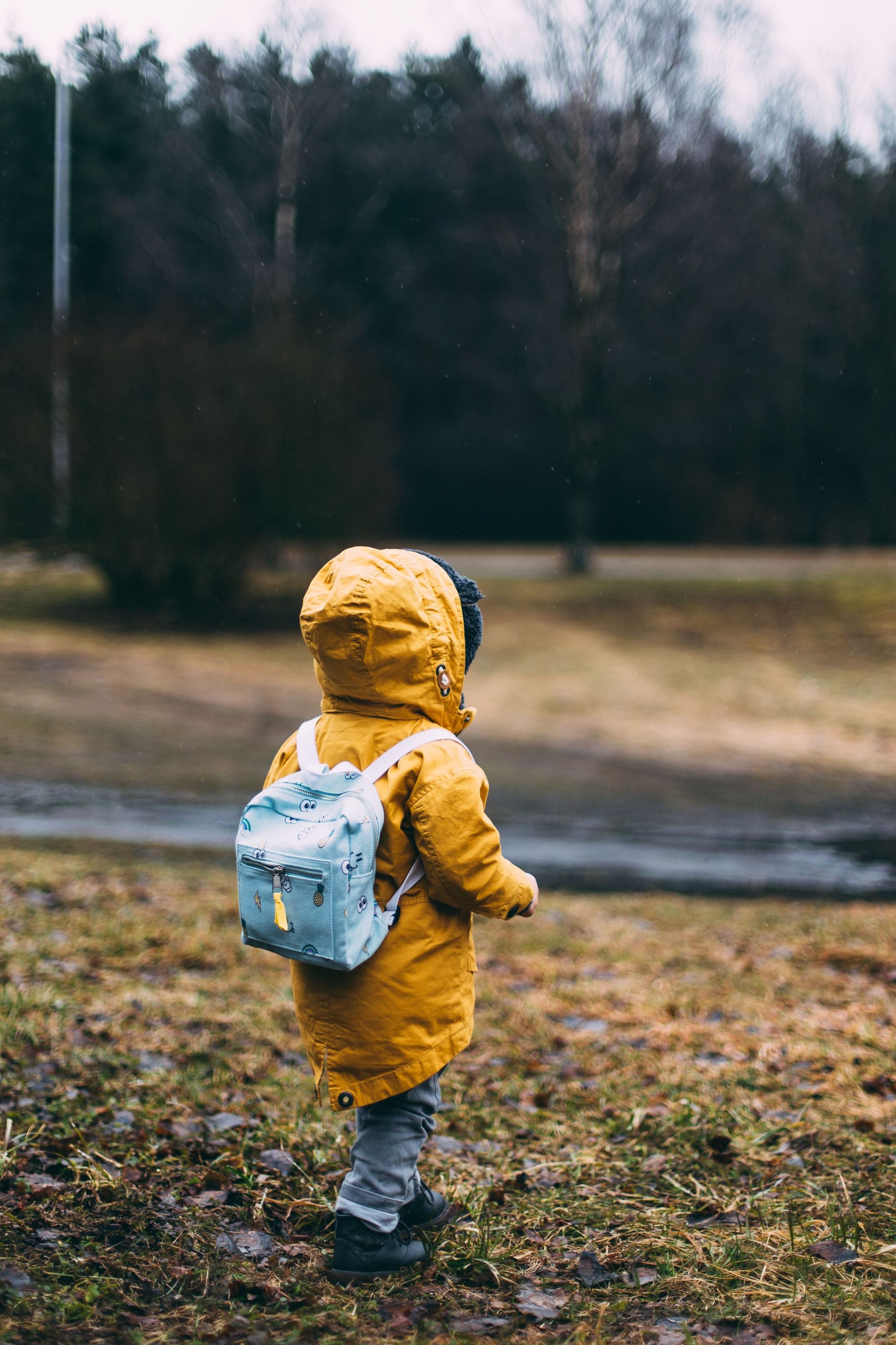 A little kid in in yellow jacket and light blue backpack.