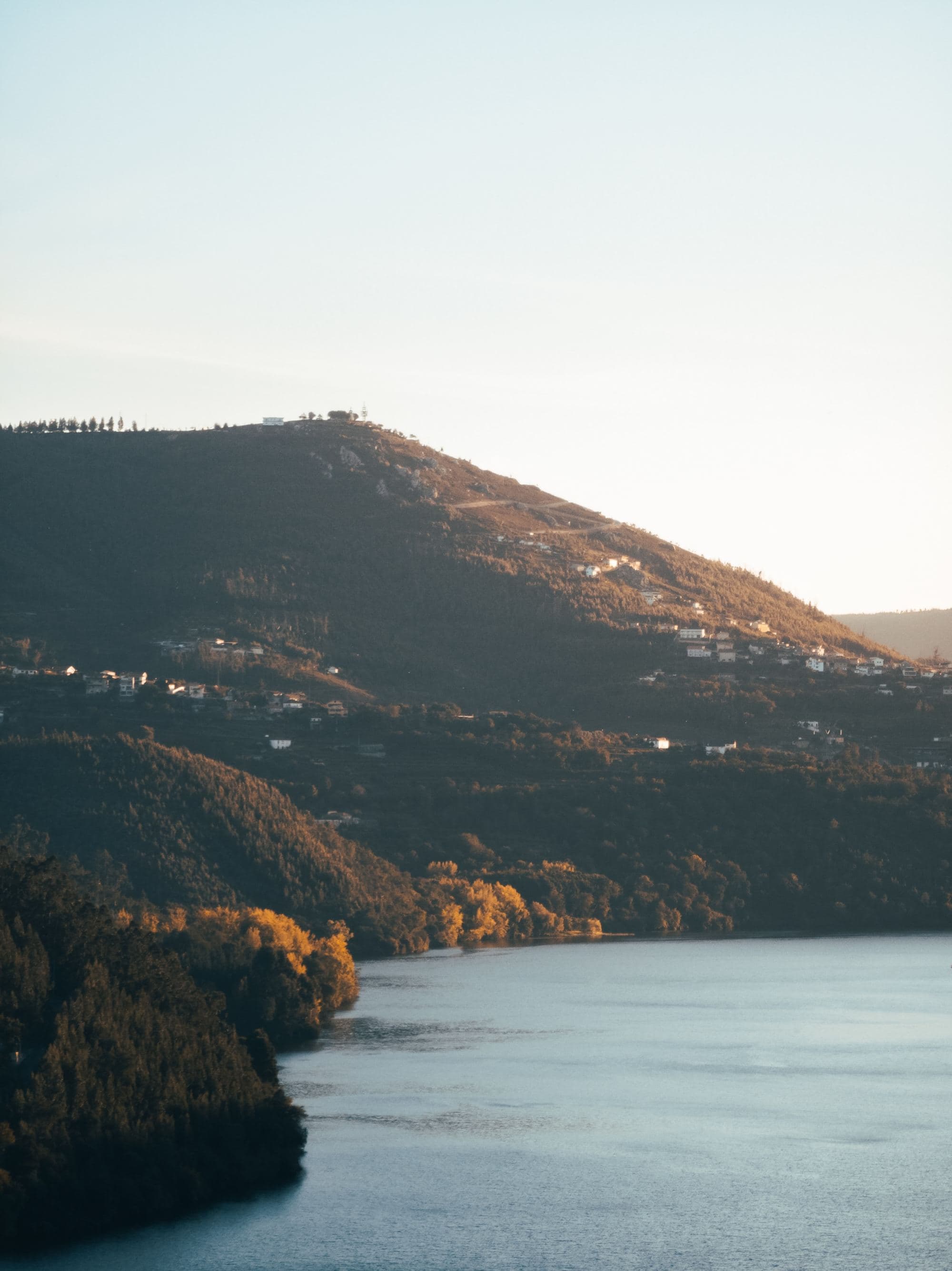 a shadowed lush hillside spotted with houses at sun set on a wide river