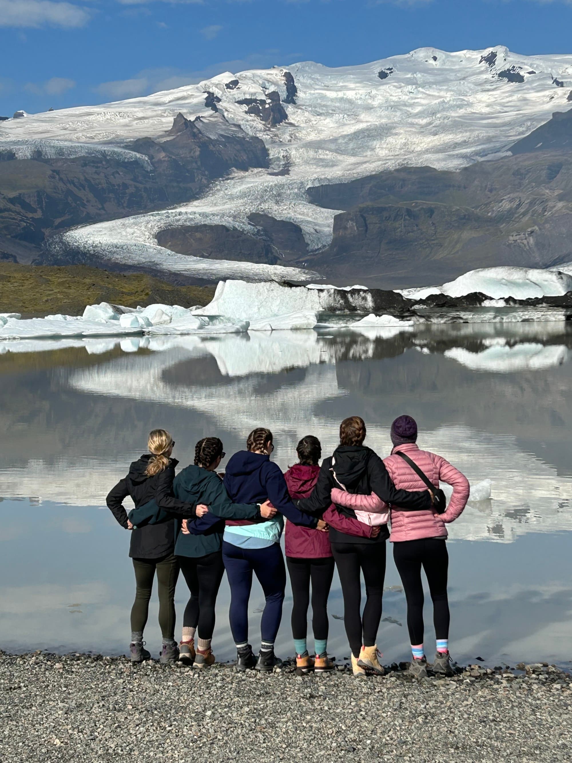 6 girls facing a lake with snow covered mountains.