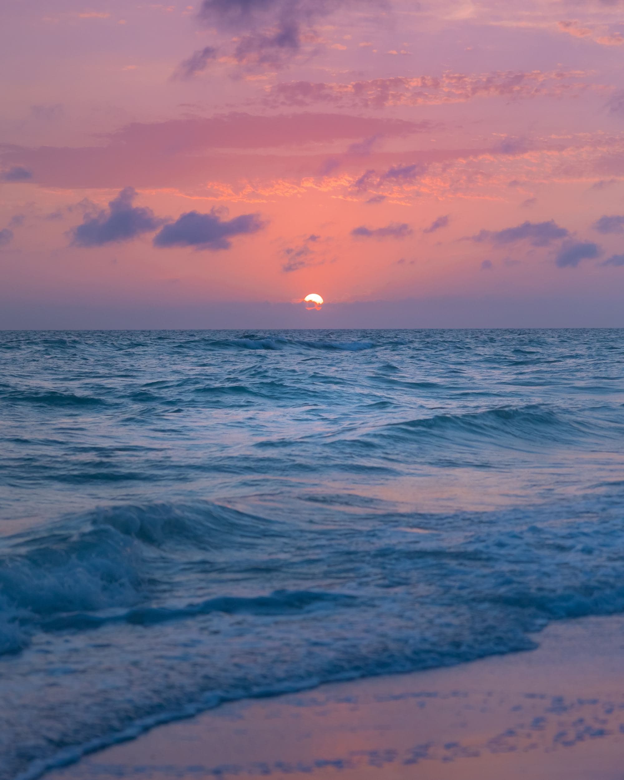 a final peak at the white sun during a pink and purple sunset over the ocean