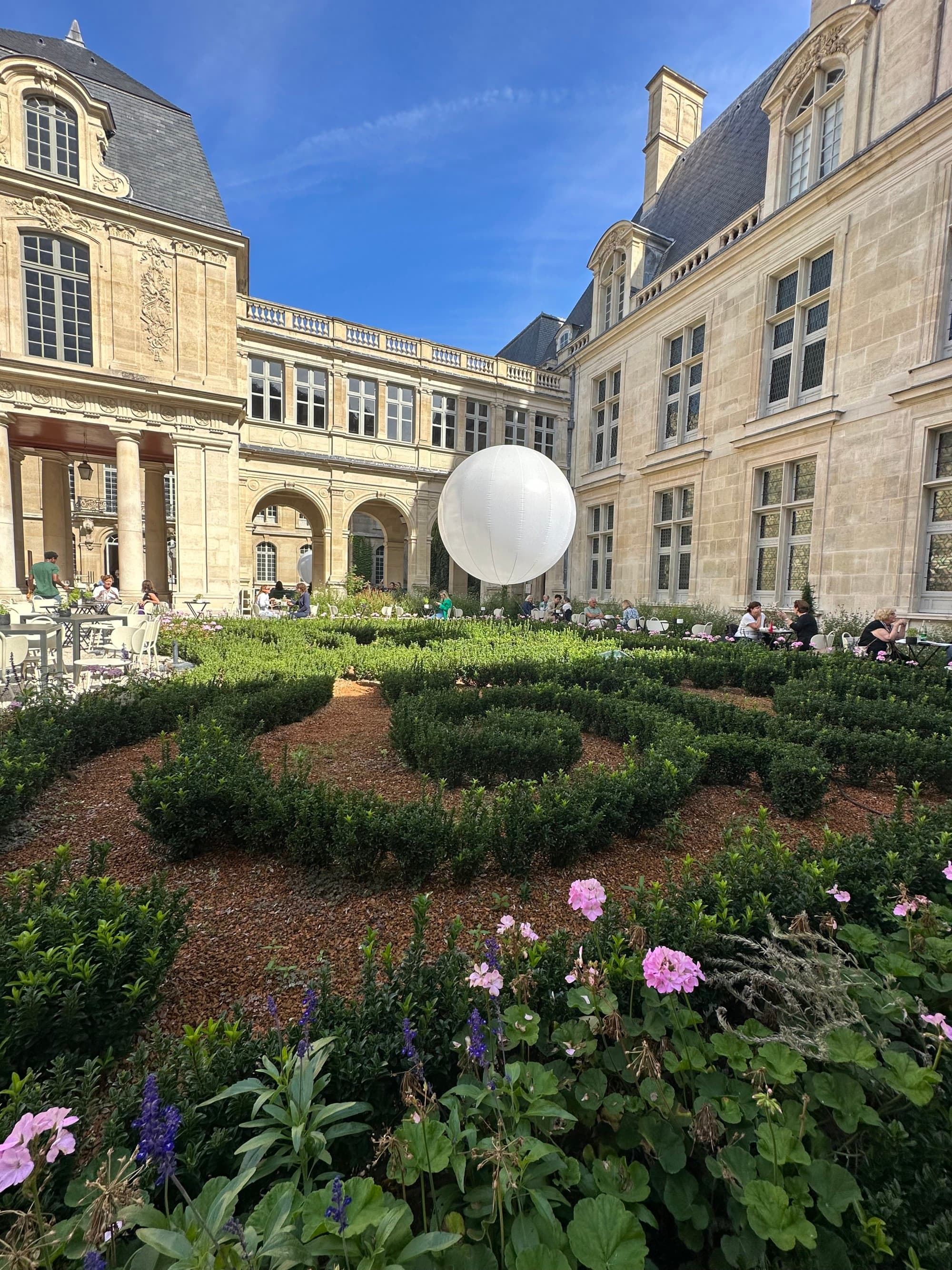 A garden with an architectural balloon surrounded by a beige French-style building during daytime.