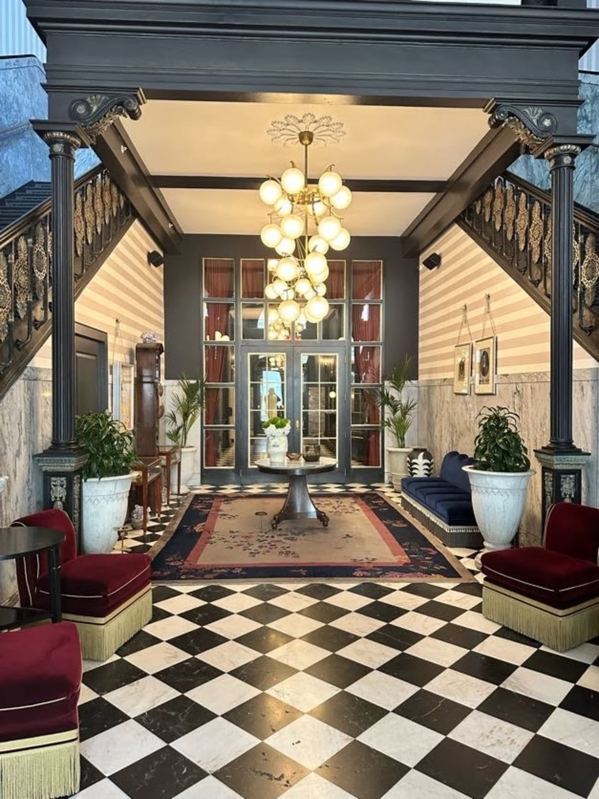 This image showcases an elegant and luxurious interior hallway with a checkered floor, ornate staircase, and stylish furniture.