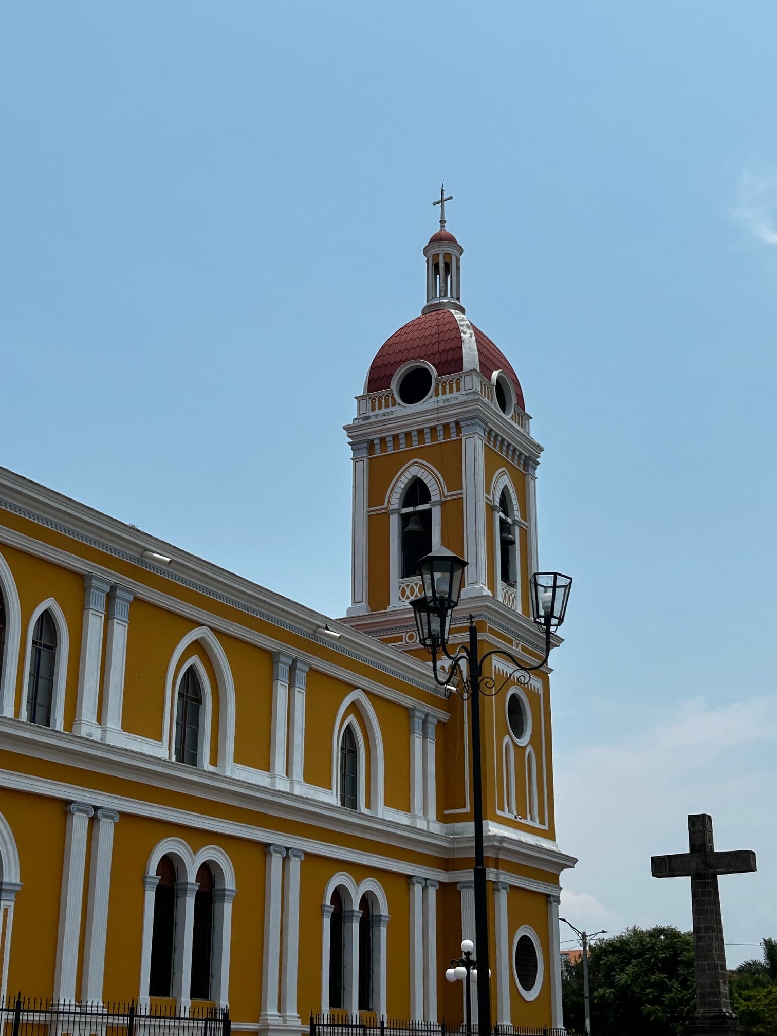 A beautiful yellow and white church with a dome and a cross to the right of it near a street lamp.