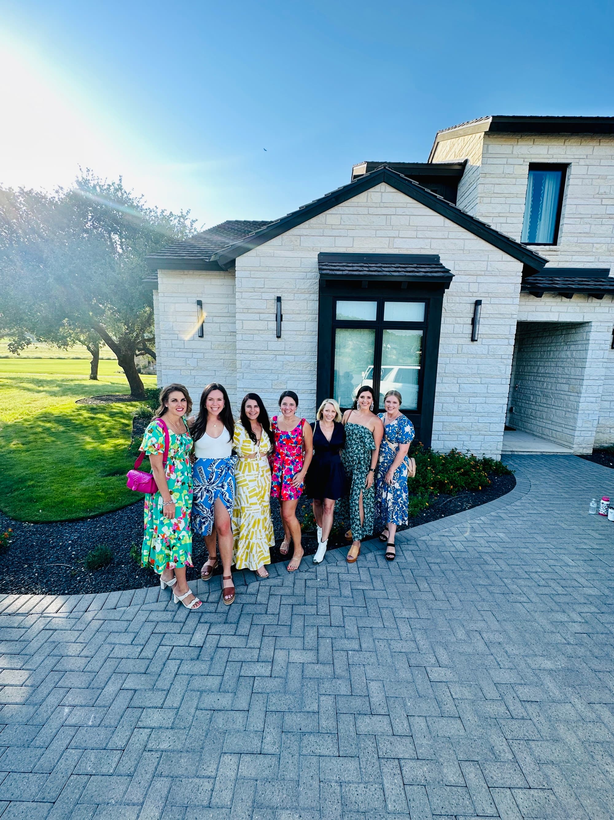 A group of women posing outdoors in front of a white building.
