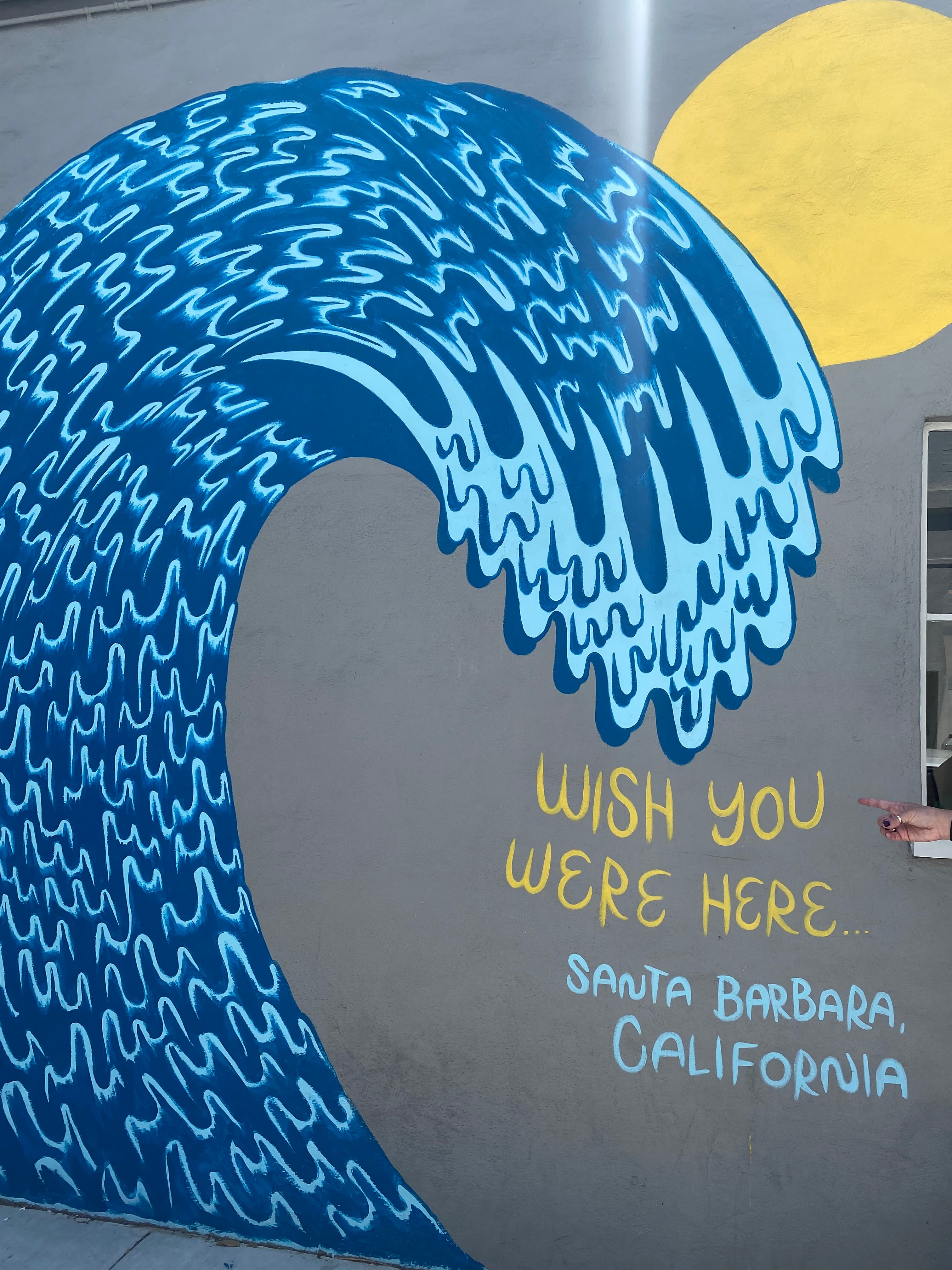 A mural of a blue wave that says "Wish you were here... Santa Barbara California" in blue and yellow lettering.