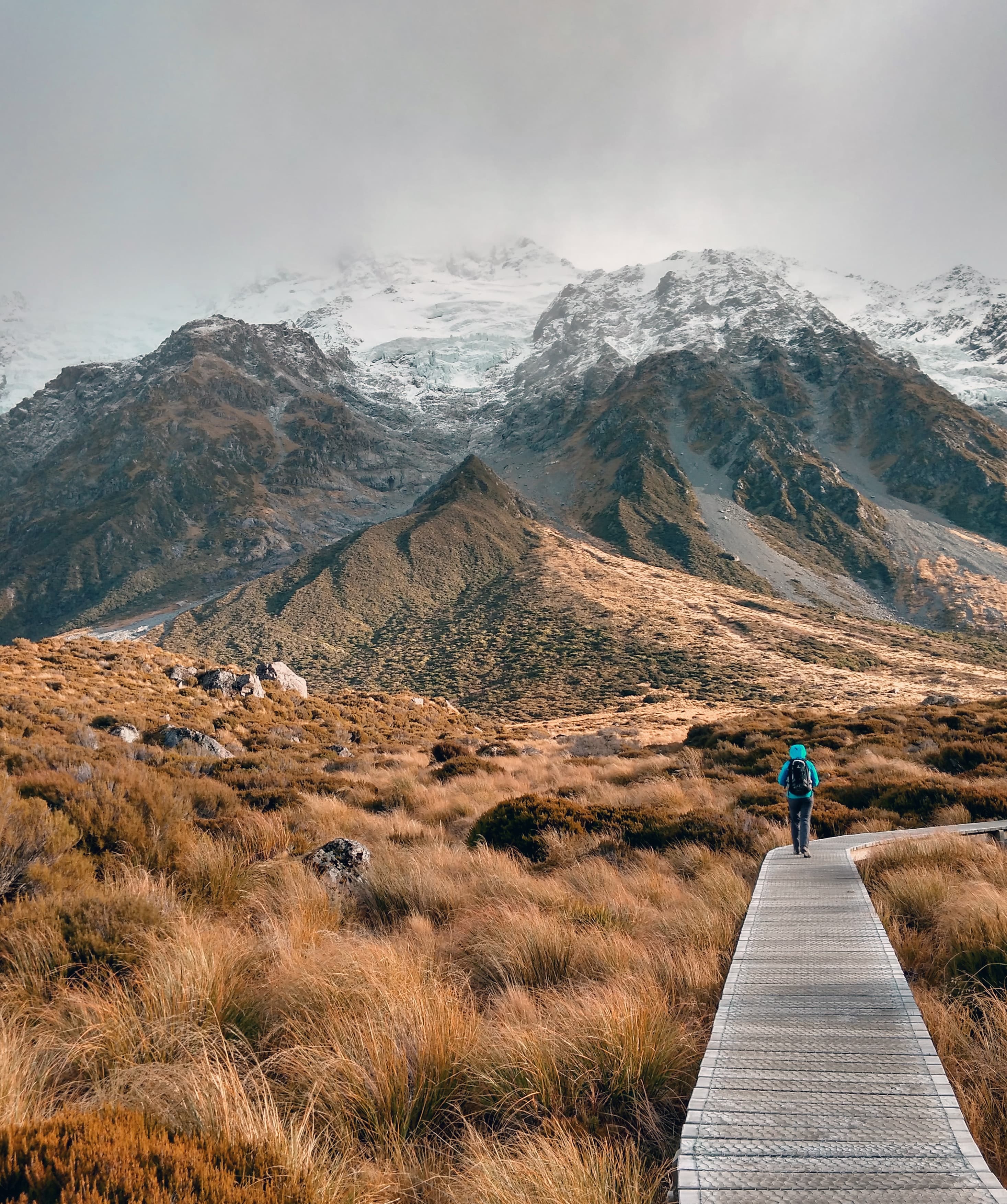 Person walking on wood path next to valley and snow-covered mountains