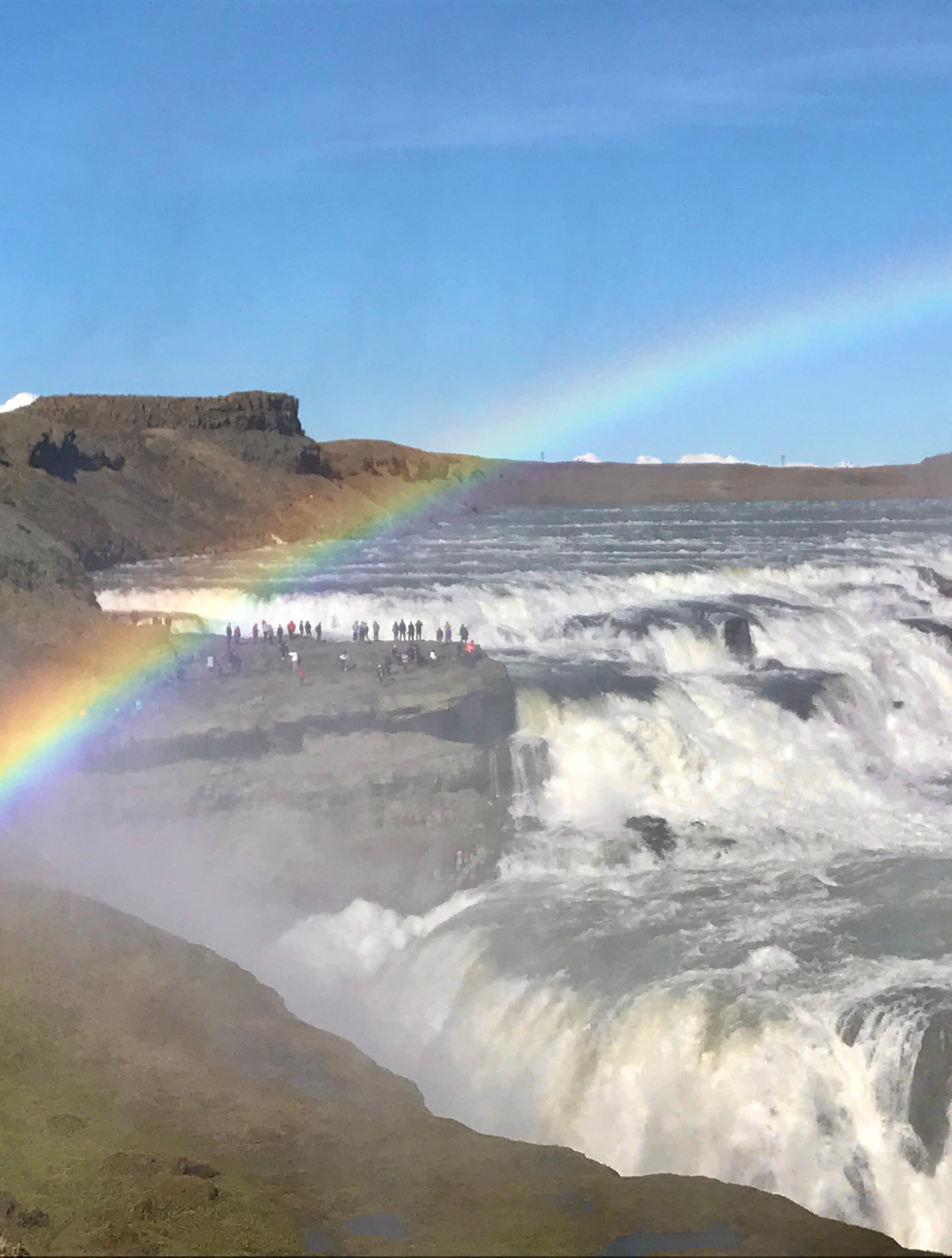 A view of the beach with a rainbow in the distance on a sunny day.