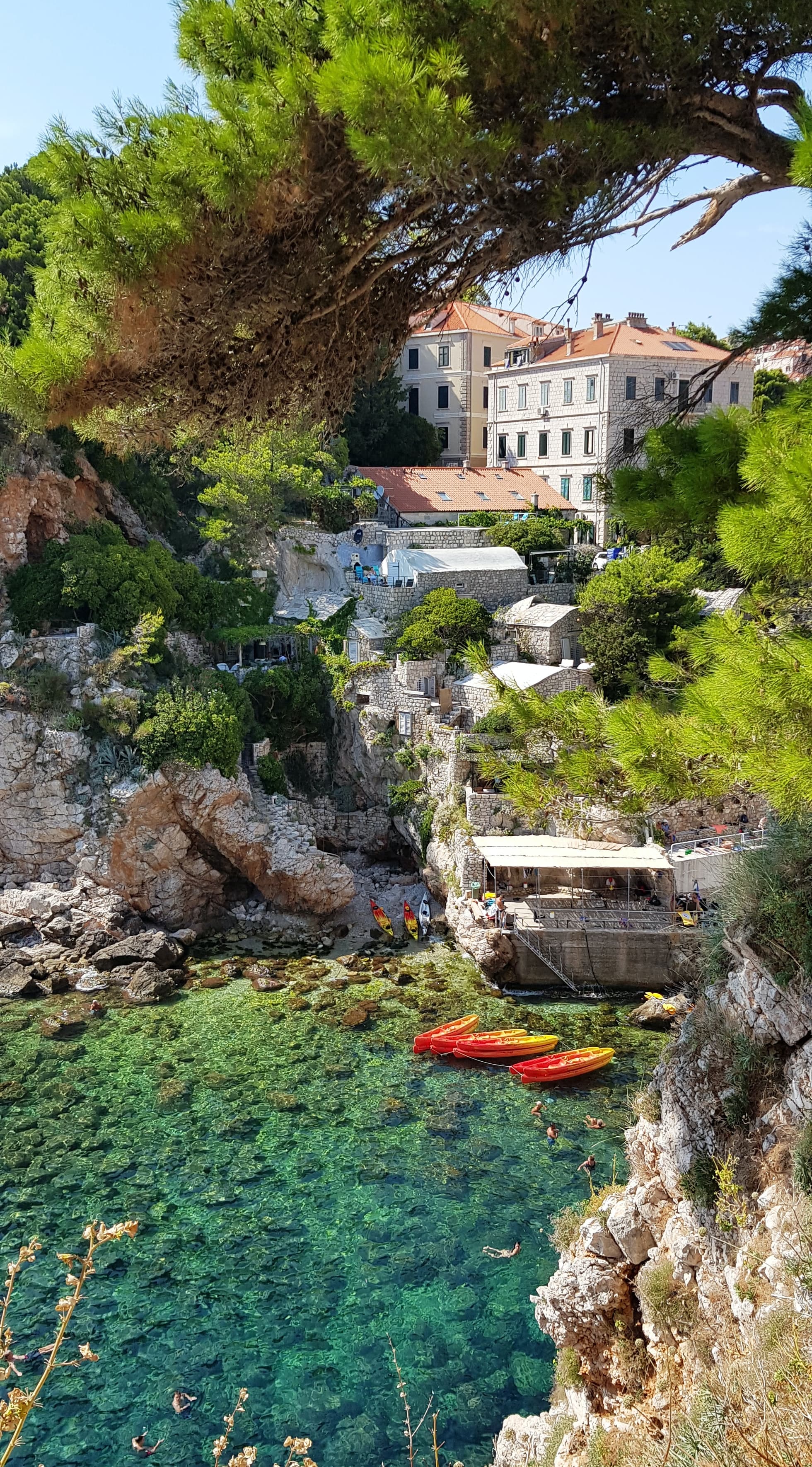 rocky cliff with buildings into clear waters with kayaks