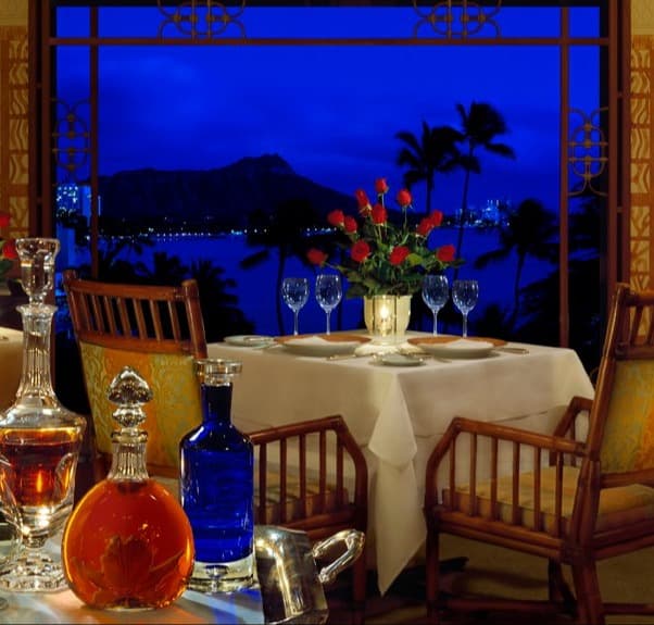A white table with red roses inside a restaurant overlooking the ocean with an island in the distance at one of the best restaurants Oahu.