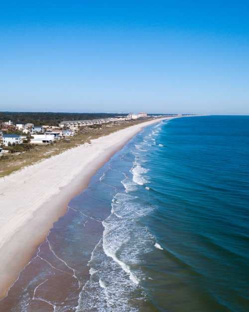 View of the coastline with white sand beaches and calm blue waves washing on the beach on a sunny day.