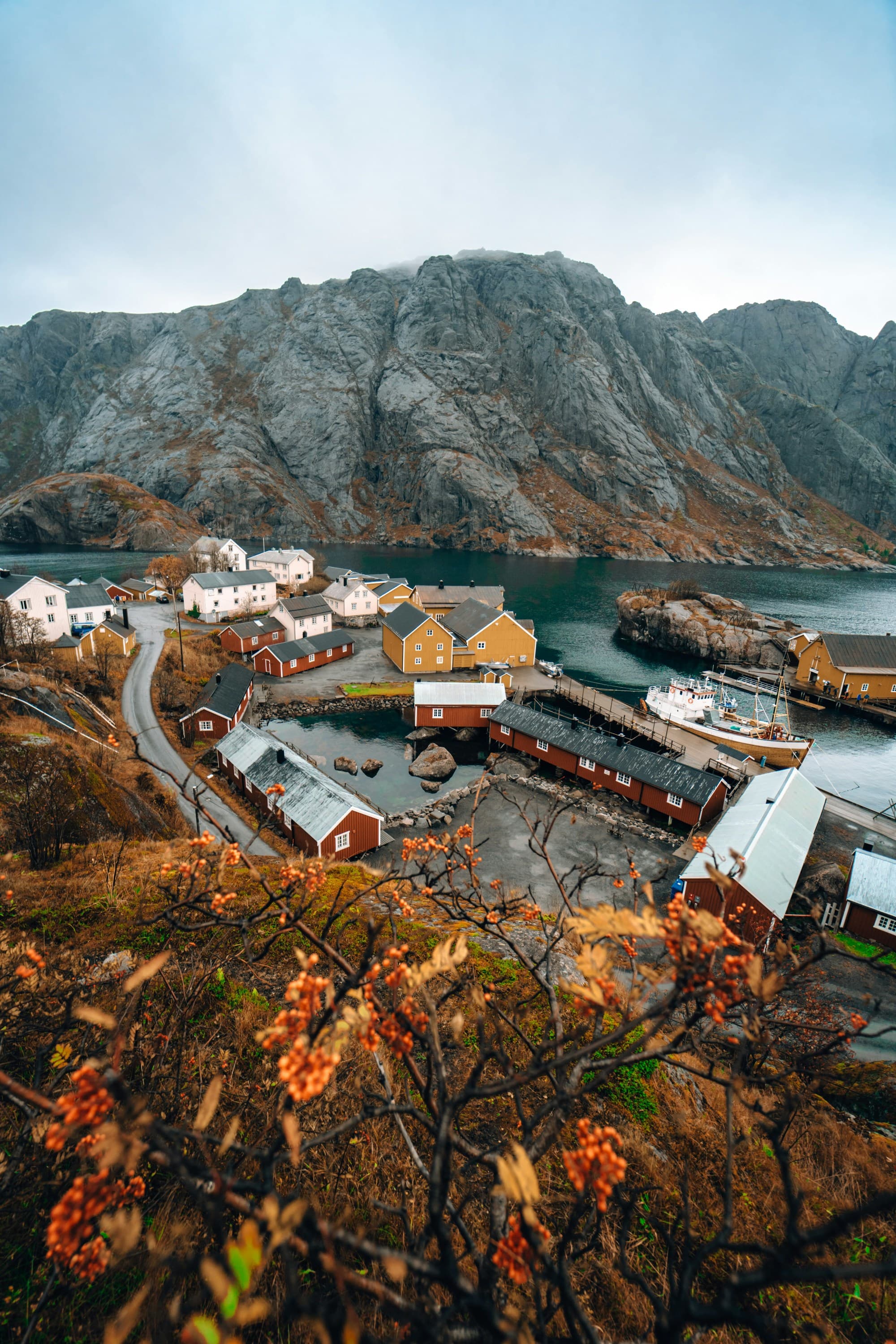 The image portrays a scenic coastal village with colorful buildings nestled between a mountain and a calm bay.