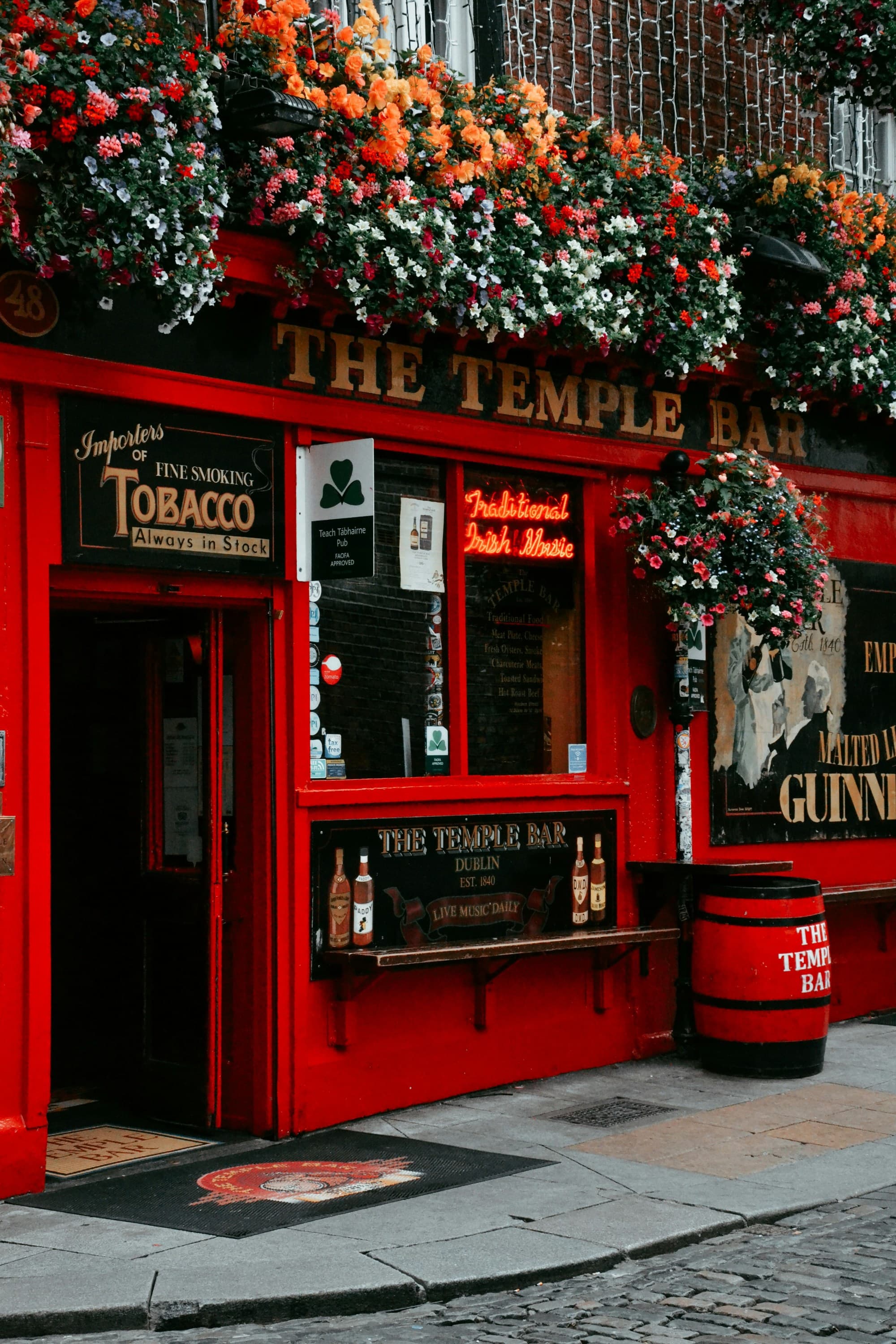 The image shows the vibrant red facade of The Temple Bar, Dublin, adorned with an abundance of colorful flowers, taken during a pub crawl in Dublin.
