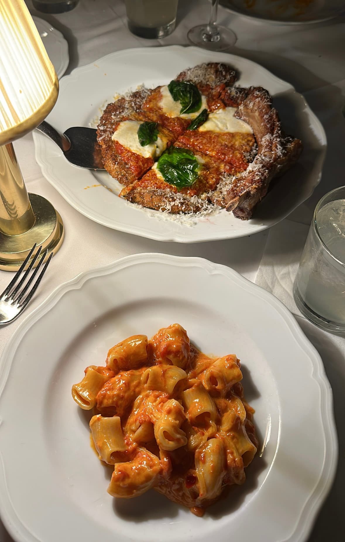 Spicy rigatoni and veal parmesan plated at Carbone on a tablecloth under soft light.