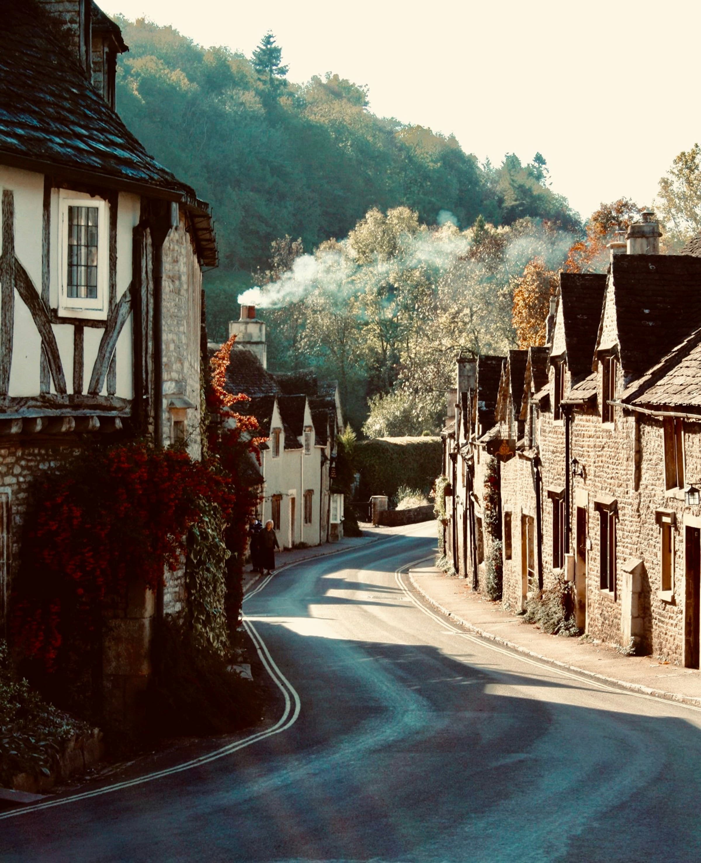 Brown brick houses at Castle Combe line the winding road as the sun sets over the hills.