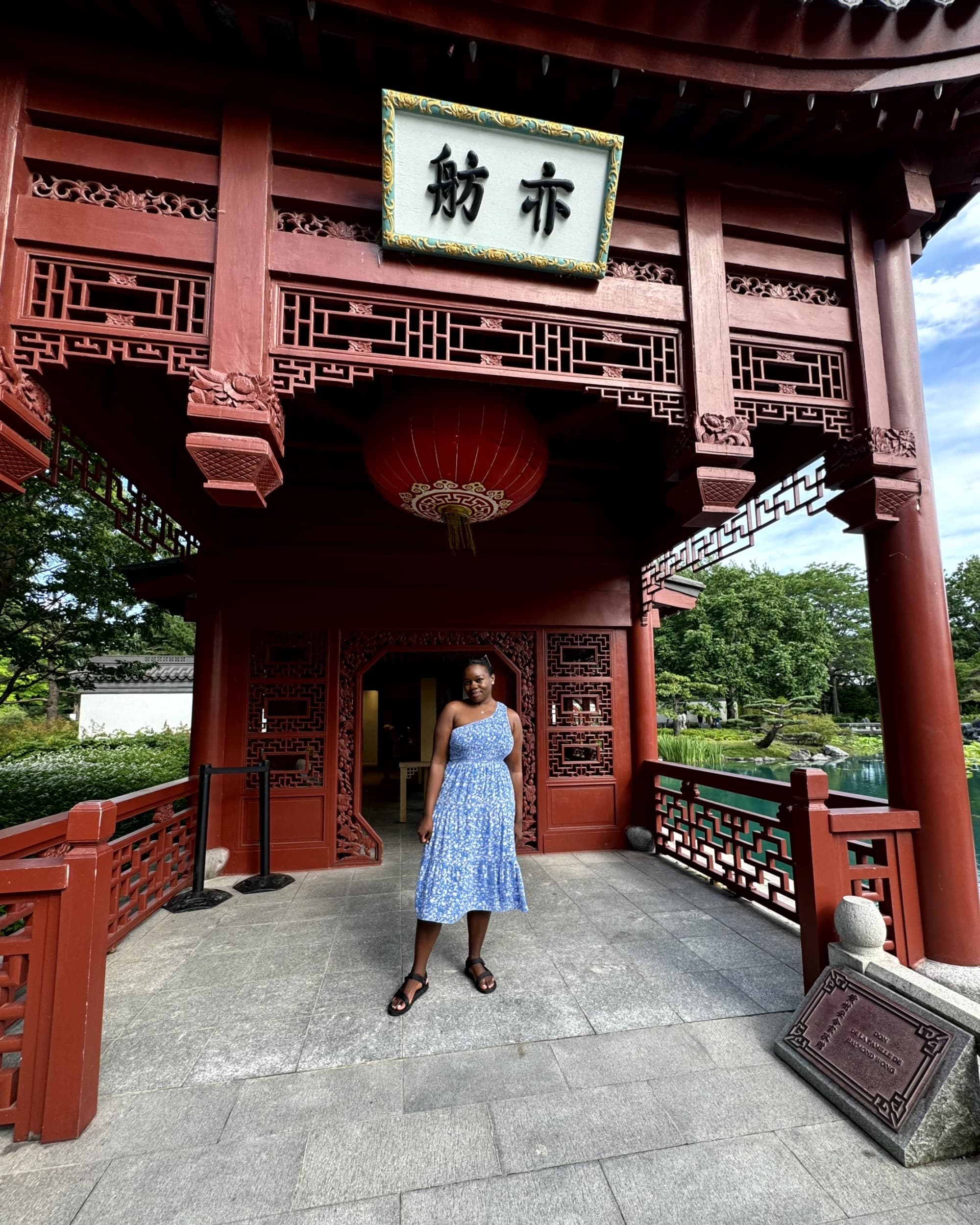 A woman under a red structure in a garden.