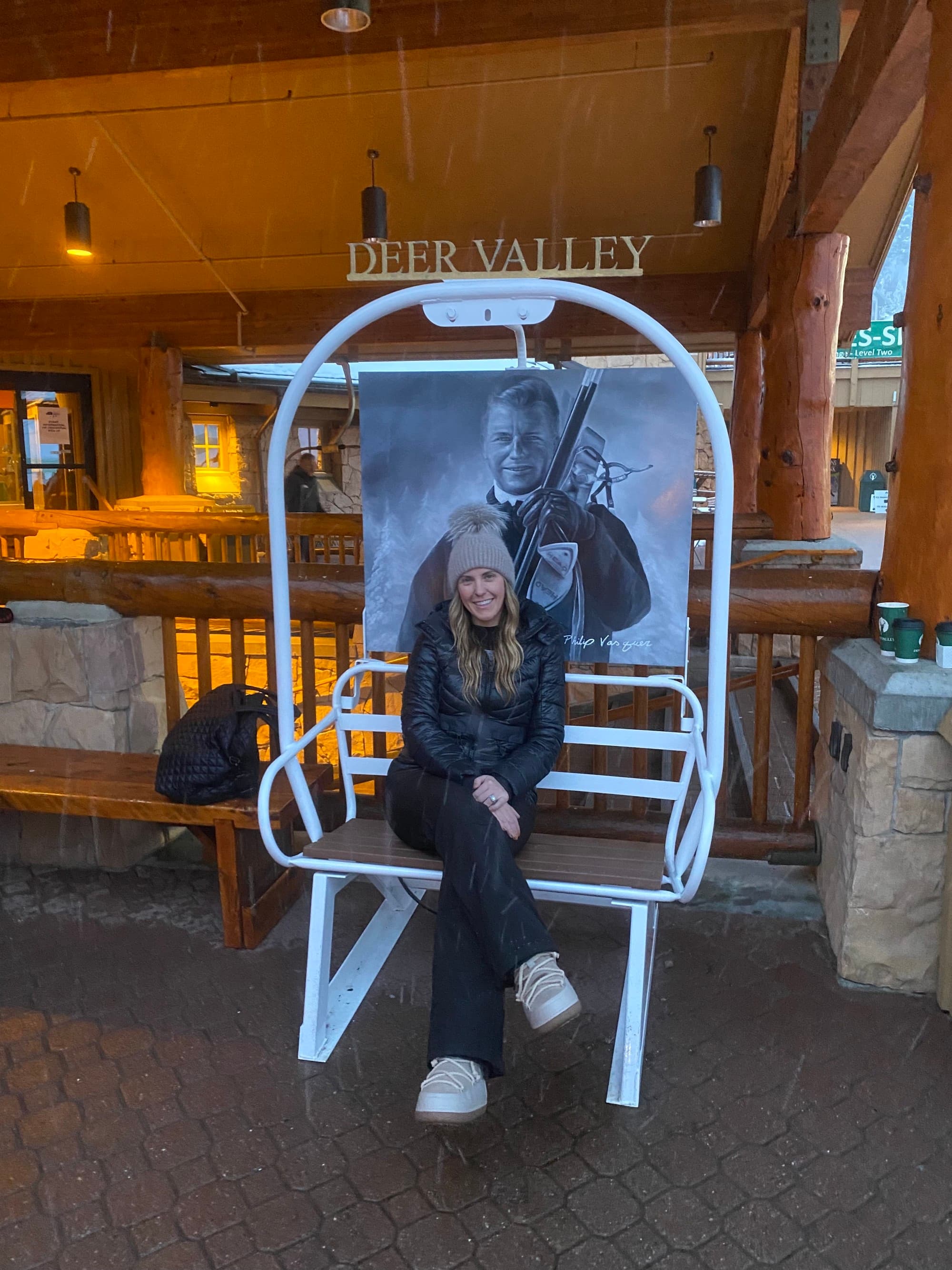 A woman sitting on a white ski chair in a lobby with a Deer Valley sign in the background.