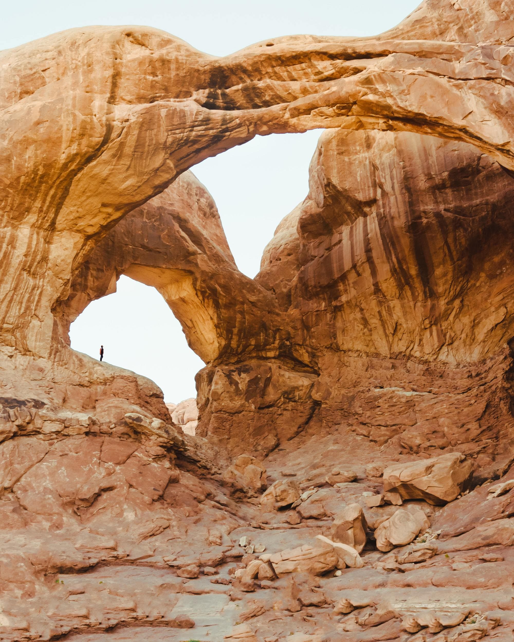 faraway view of a person standing beneath looming red rock formations