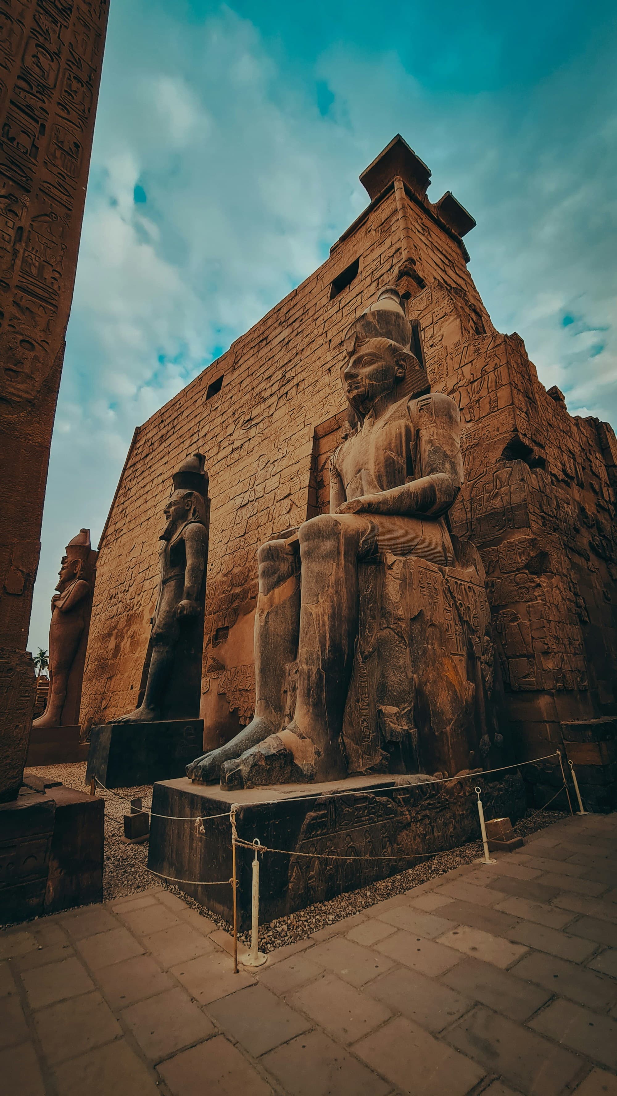 The image features grand ancient Egyptian statues seated before a temple, beneath a clear sky.
