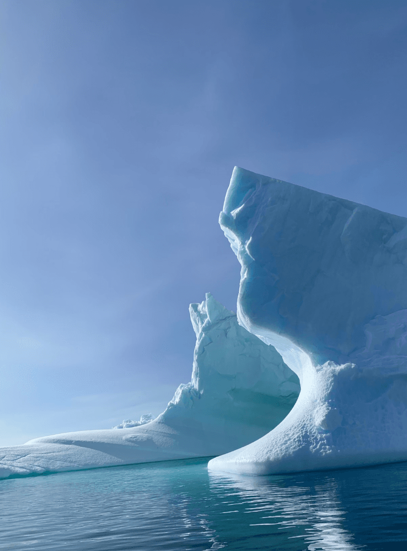 A view of a large ice berg and the turquoise blue water under a blue sky.