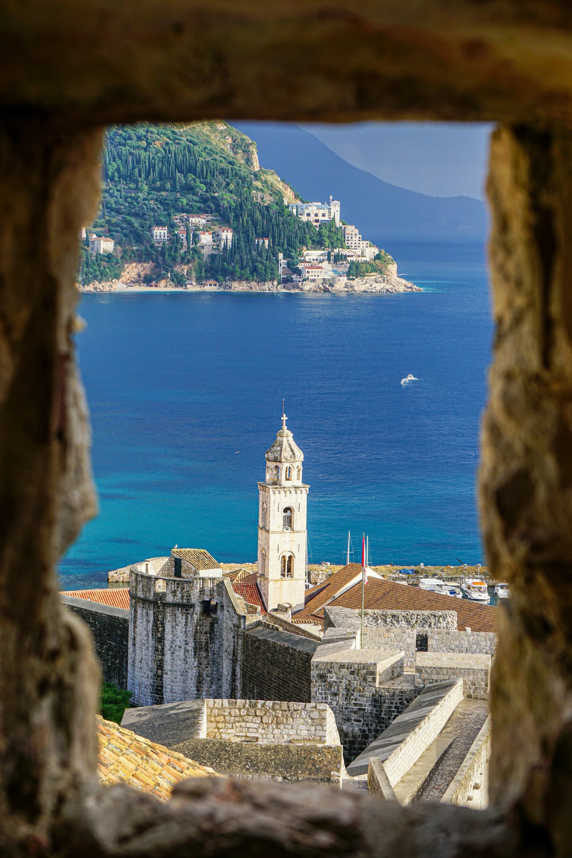 A view of a white tower from a stone window with blue water and mountains in the background.