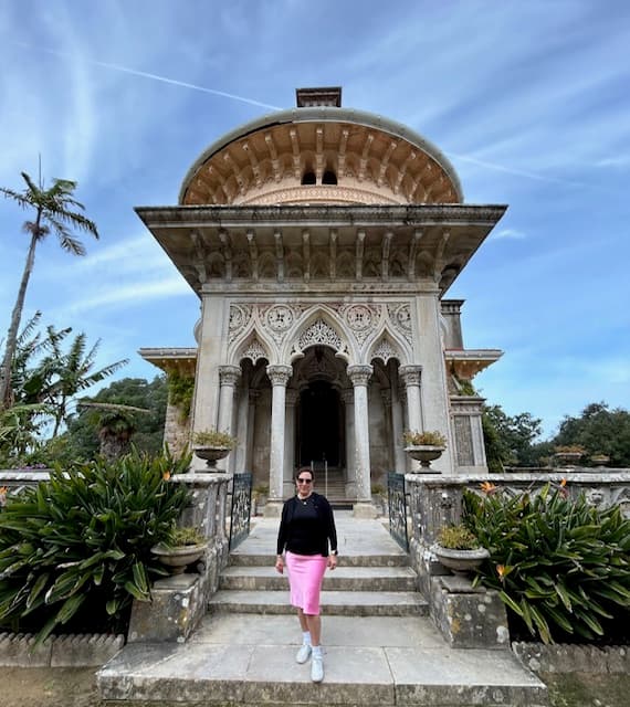 Mindy in a black top and pink skirt in front of Monserrate Palace Sintra, an ornate building with narrow columns - Mindy Levin