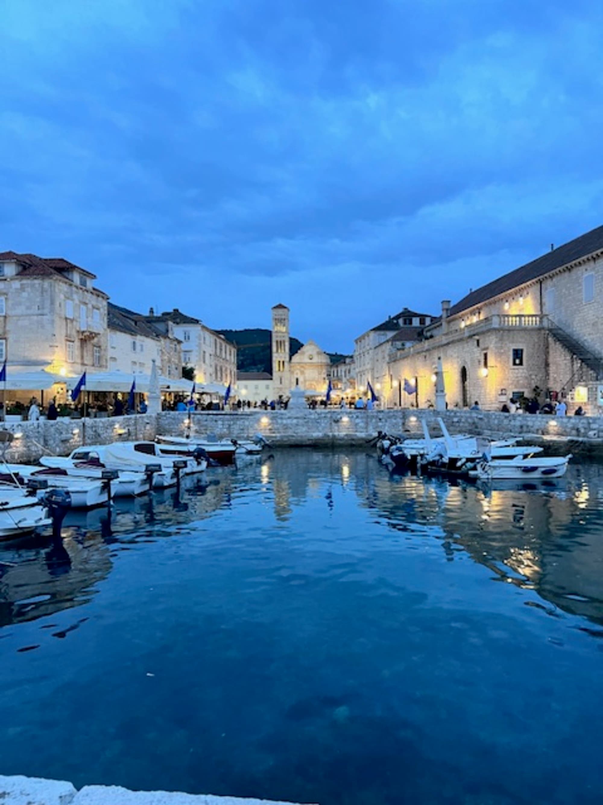 A picturesque twilight scene of a town by the water, with buildings casting reflections on the calm surface.