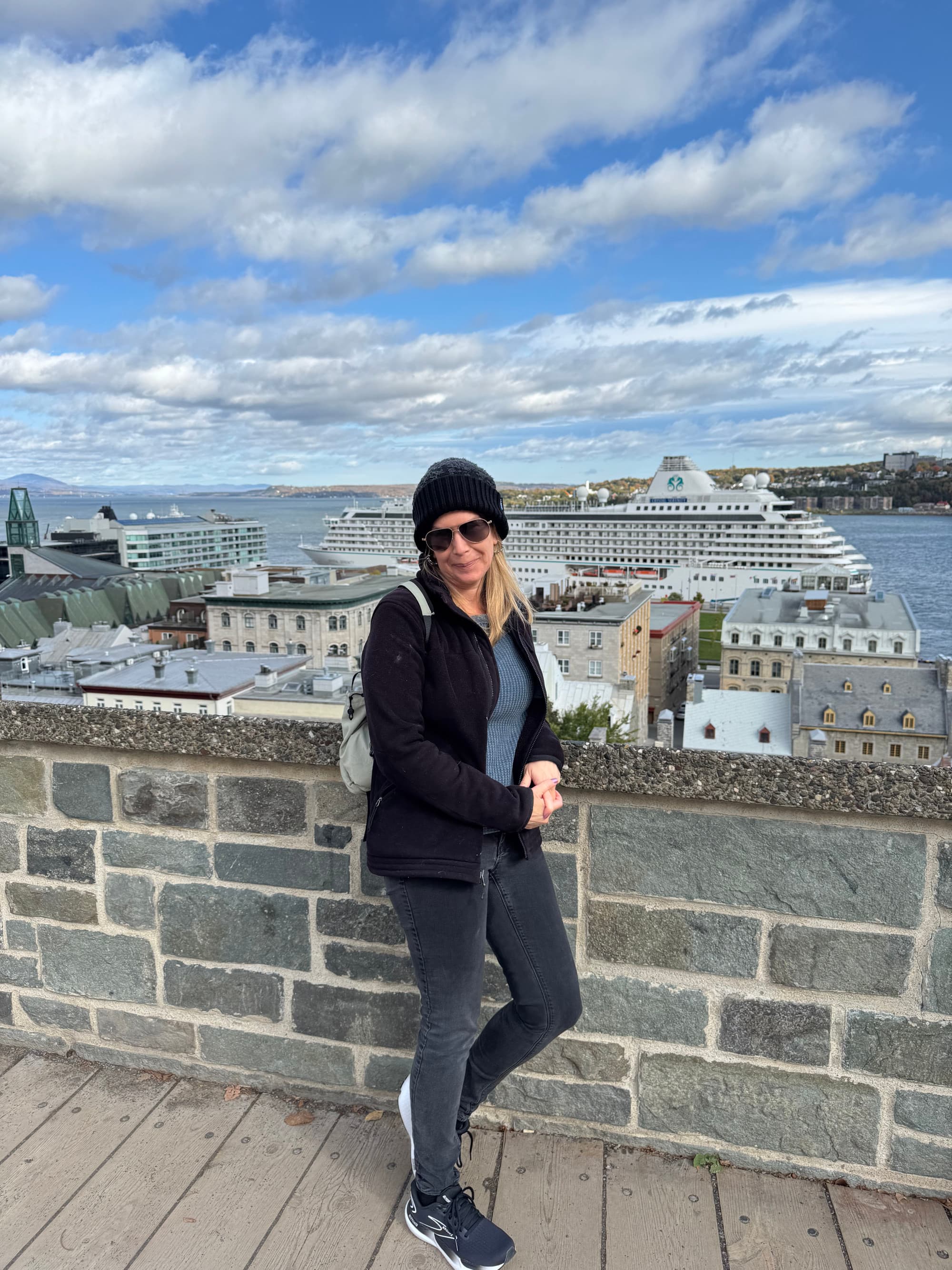 A person standing next to a brick wall with a view of a cruise ship in the water in the background