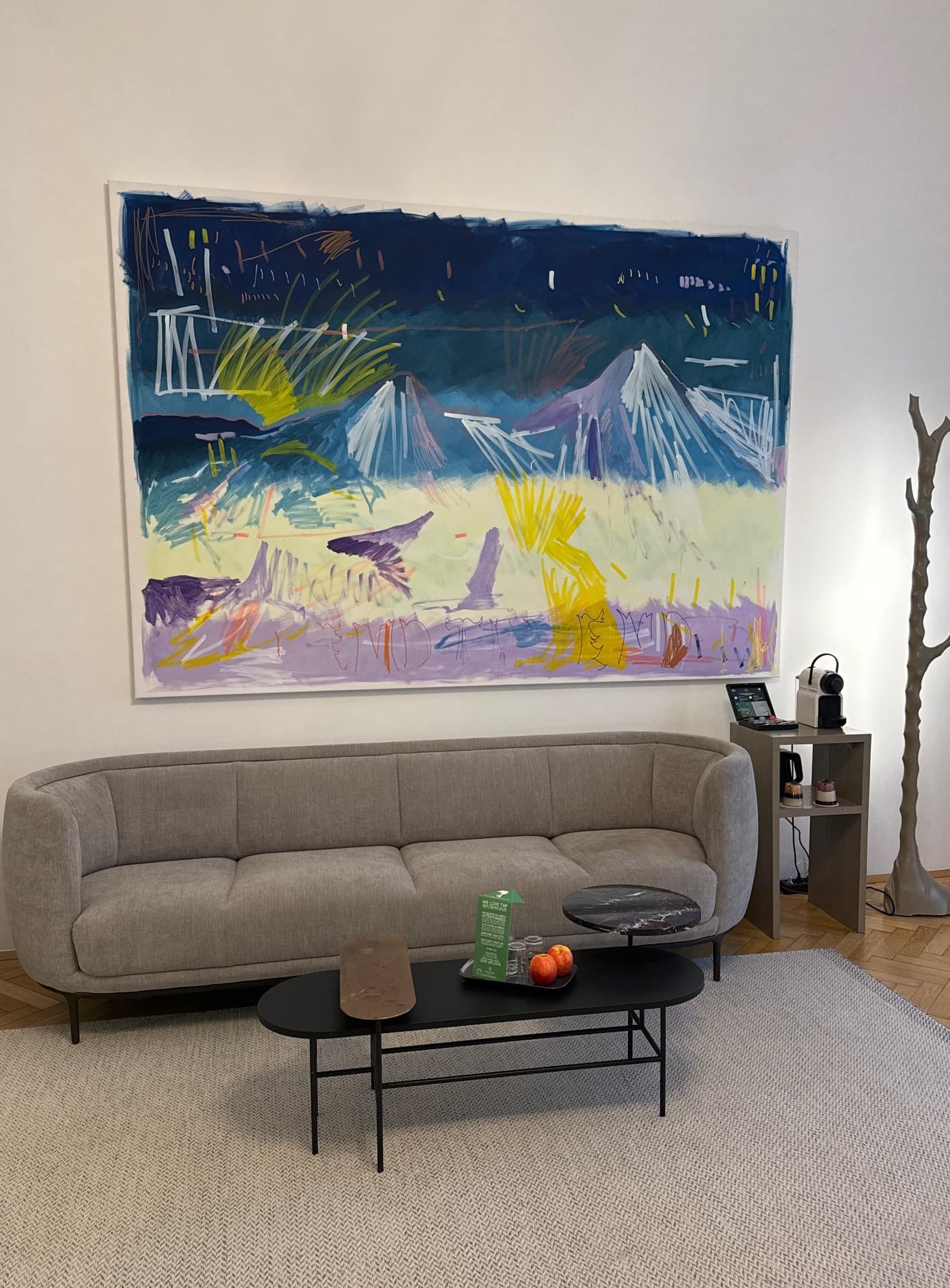 A large piece of artwork on a wall above a grey couch in a hotel room