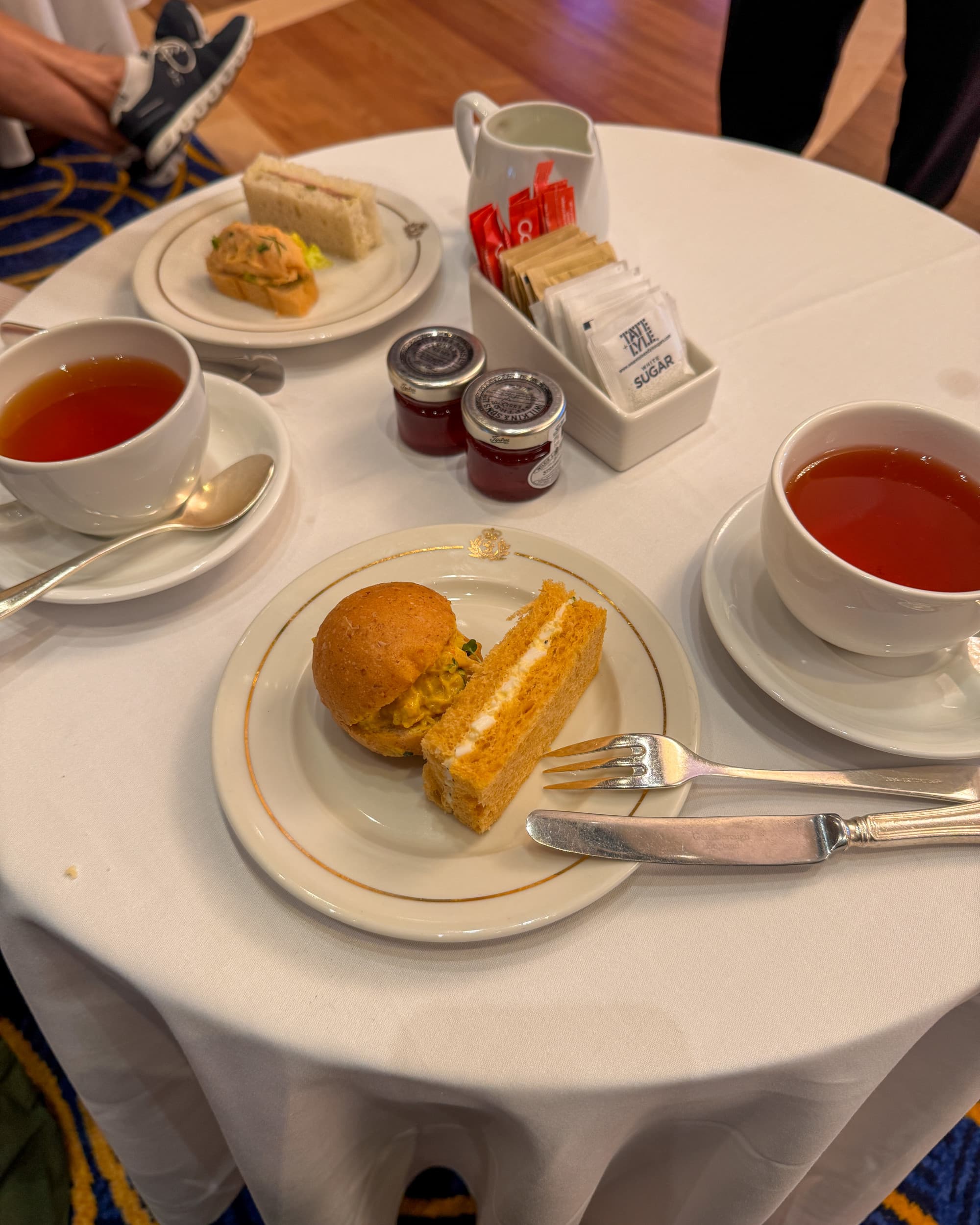 A food view of tea time, with two teacups and small bites on a table with a white tablecloth.
