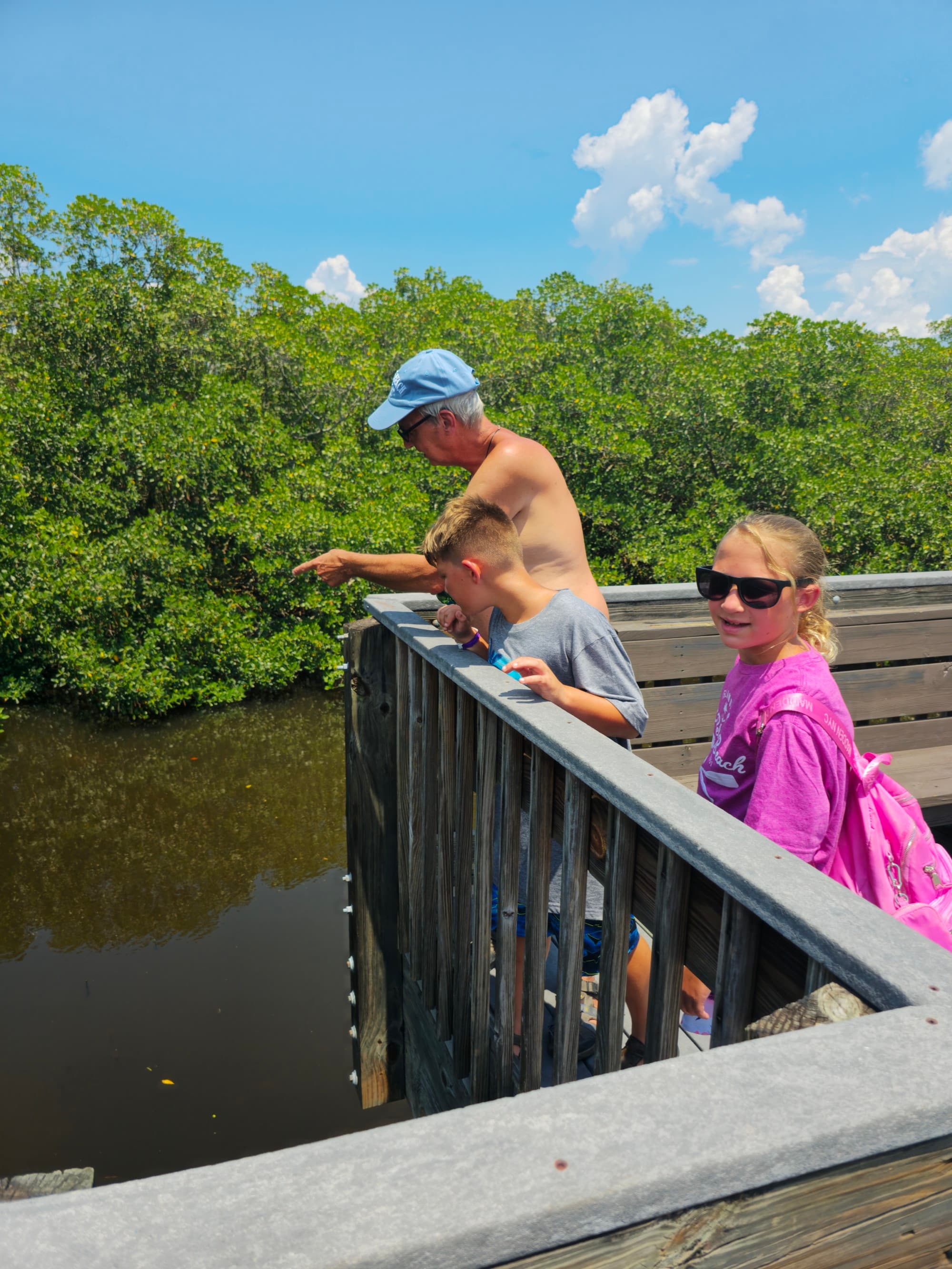 Children and a man standing on a wooden deck above a river during the daytime