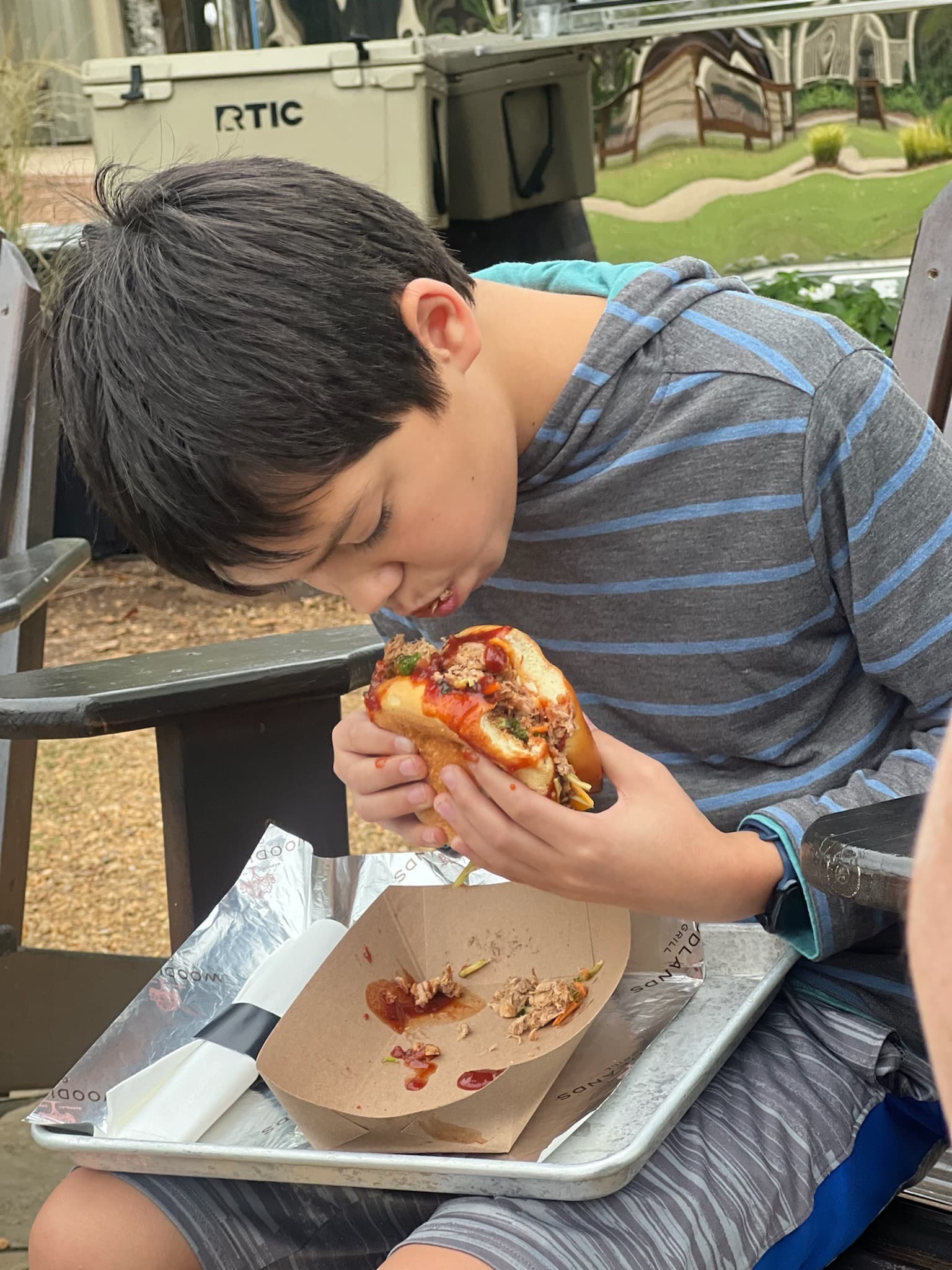 A child sitting at an outdoor bench eating a sandwich