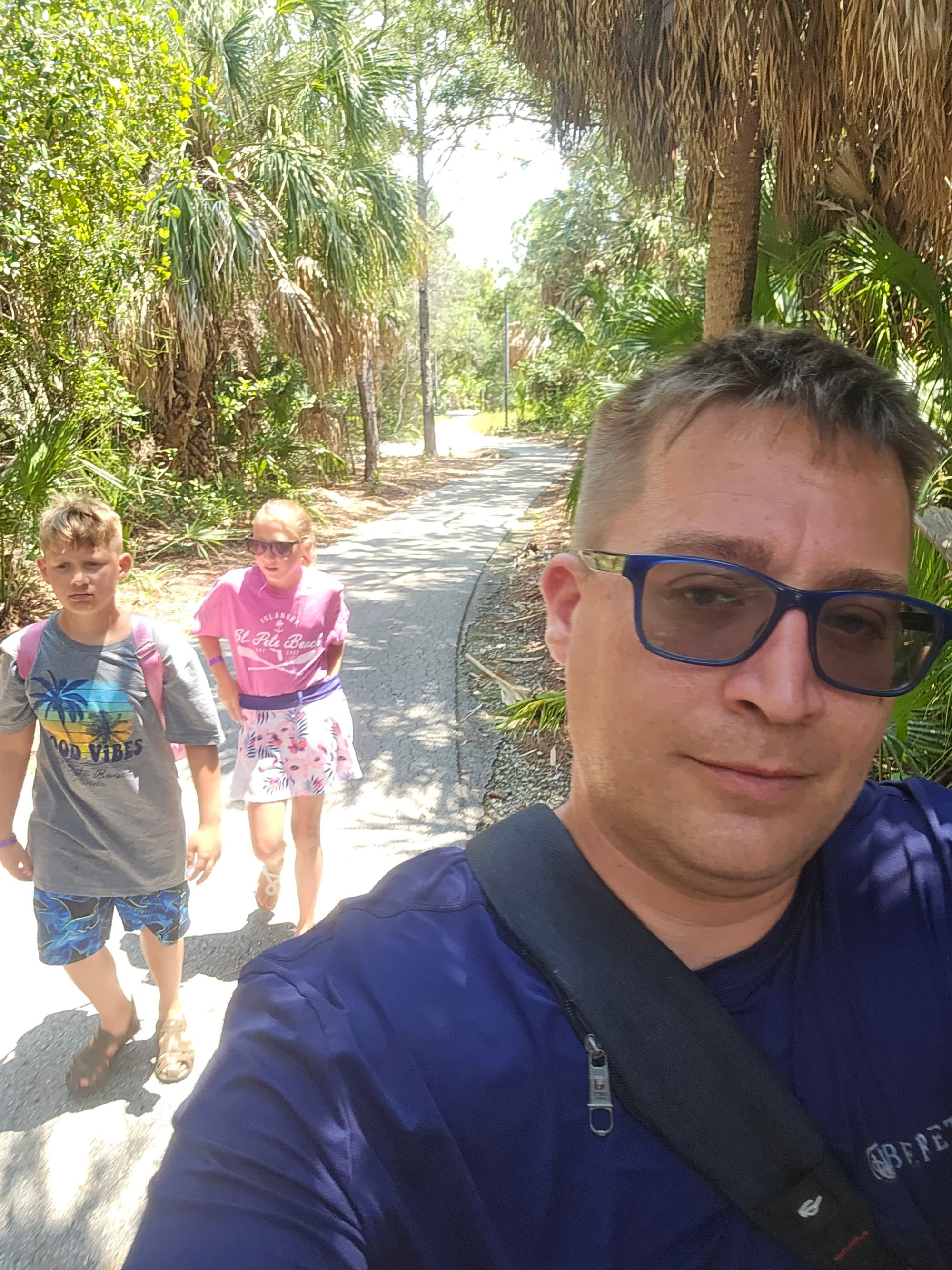A person taking a selfie photograph with children while walking on a tree lined pathway