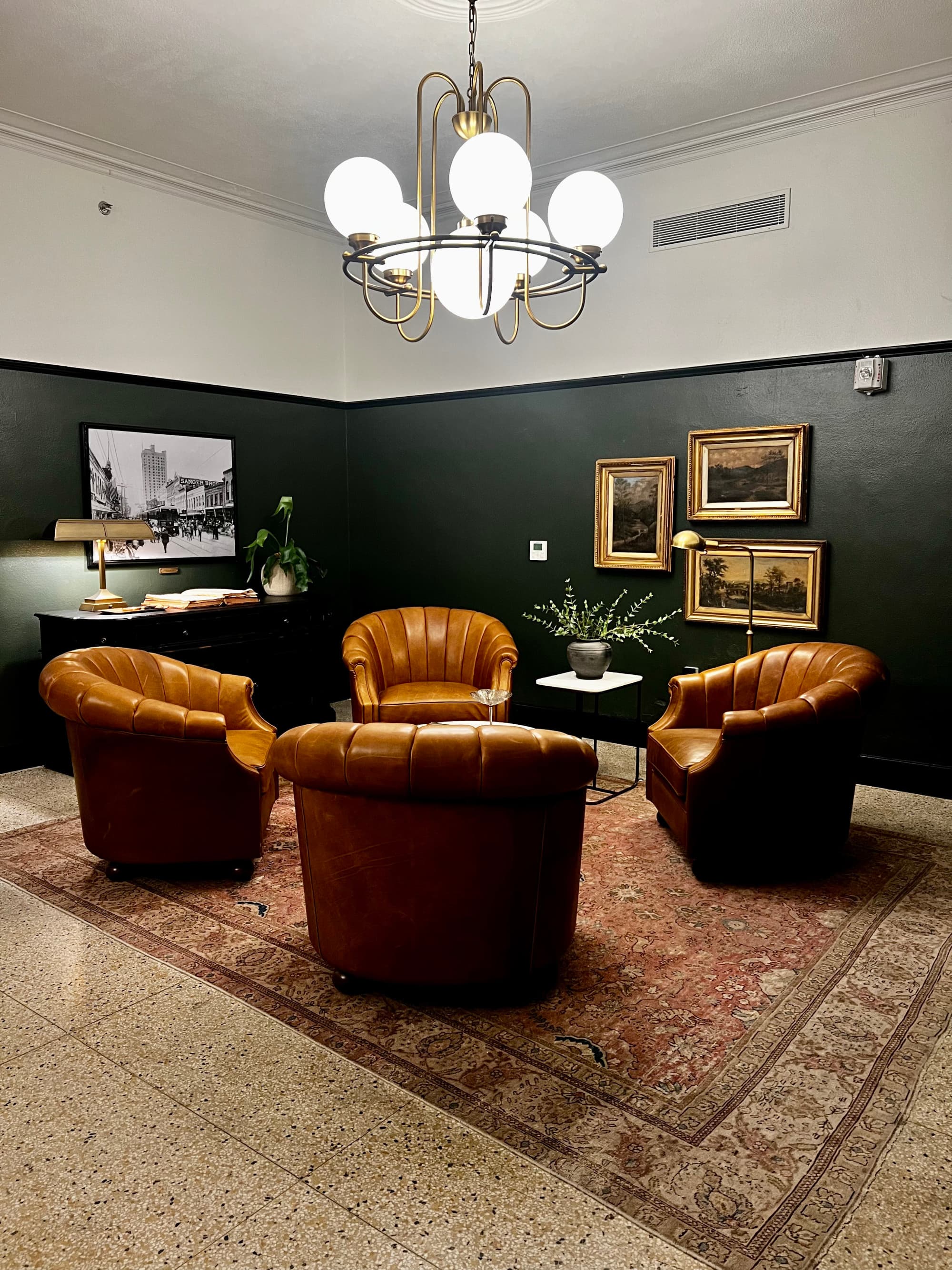 A sitting room with the walls painted black on the bottom half and white on the top with four brown leather chairs in the center of the room on a red rug.
