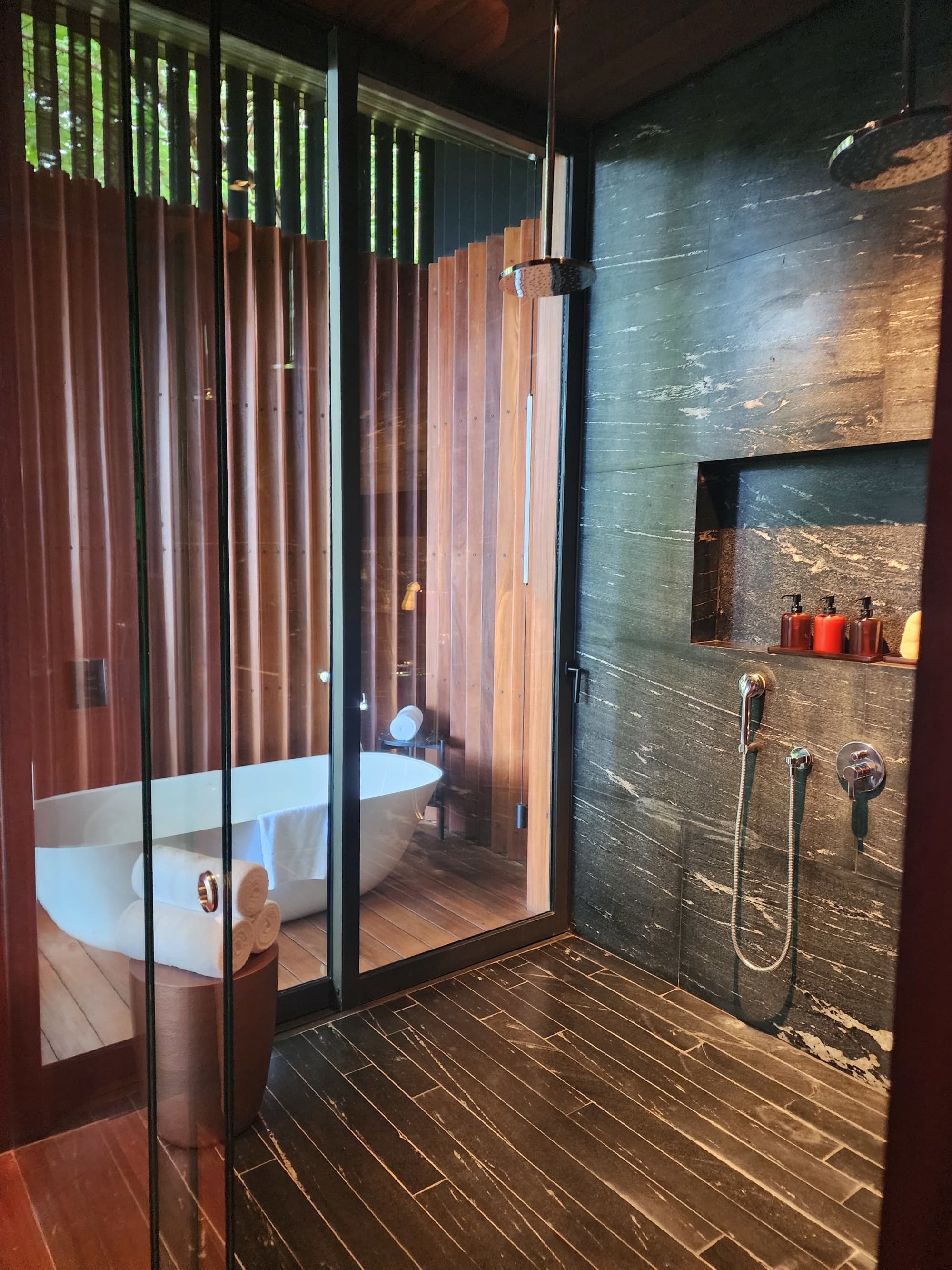 A view of the bathroom, with wood slat walls, a bath tub and shower with a serene atmosphere.