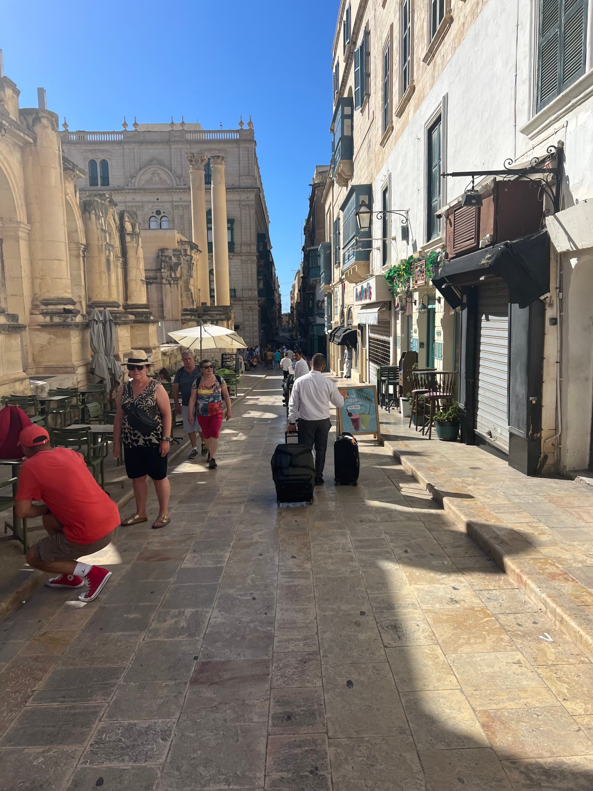 An individual rolling two suitcases down the city street.