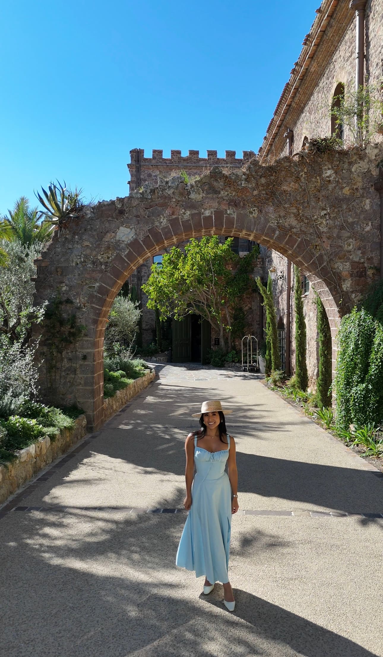 A person standing for a photograph in the middle of an outdoor walk way with an arched brick wall behind them