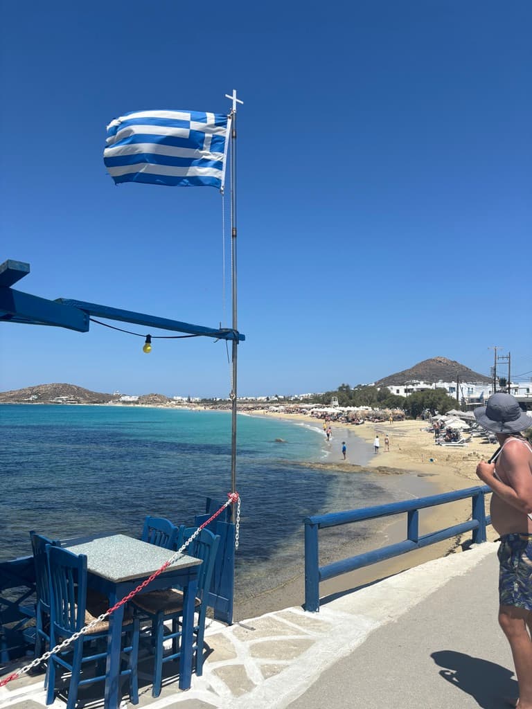 A Greek flag flag flying on a railing above the water.