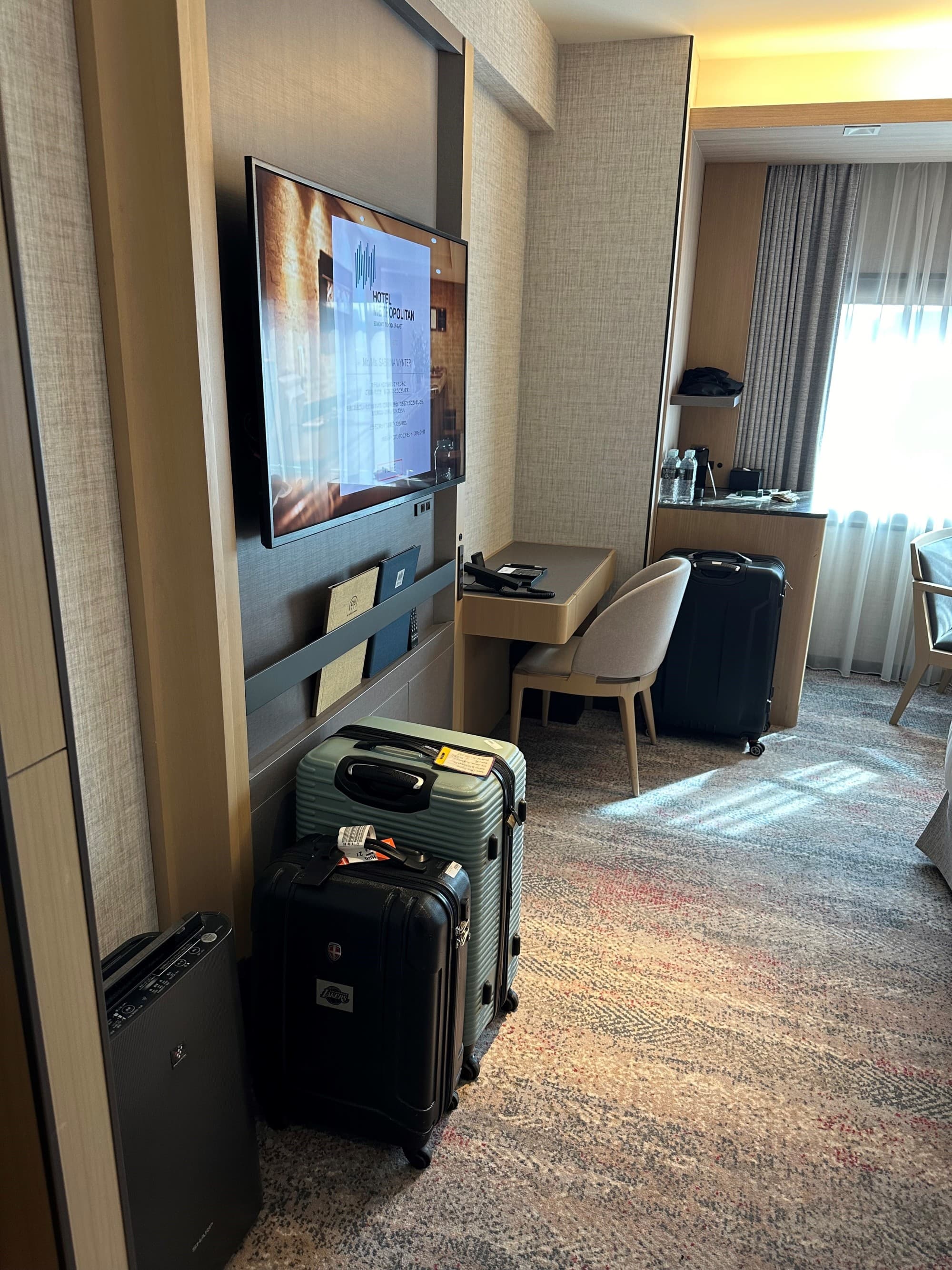 A hotel room with a tv on the wall and two suitcases standing on the floor