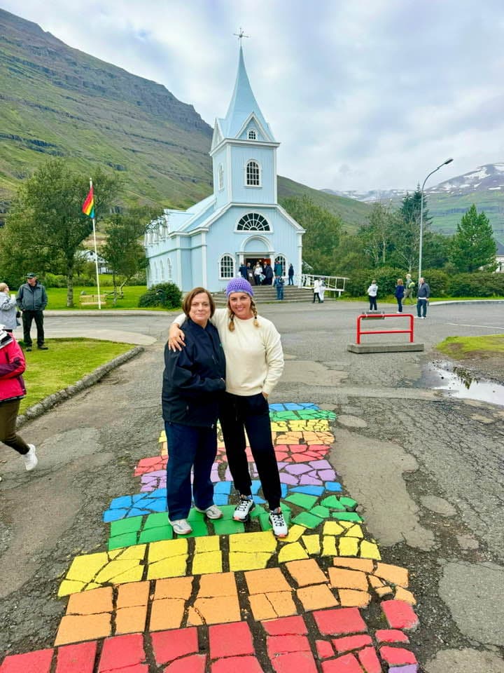 Two people standing in a rainbow-painted street during the daytime