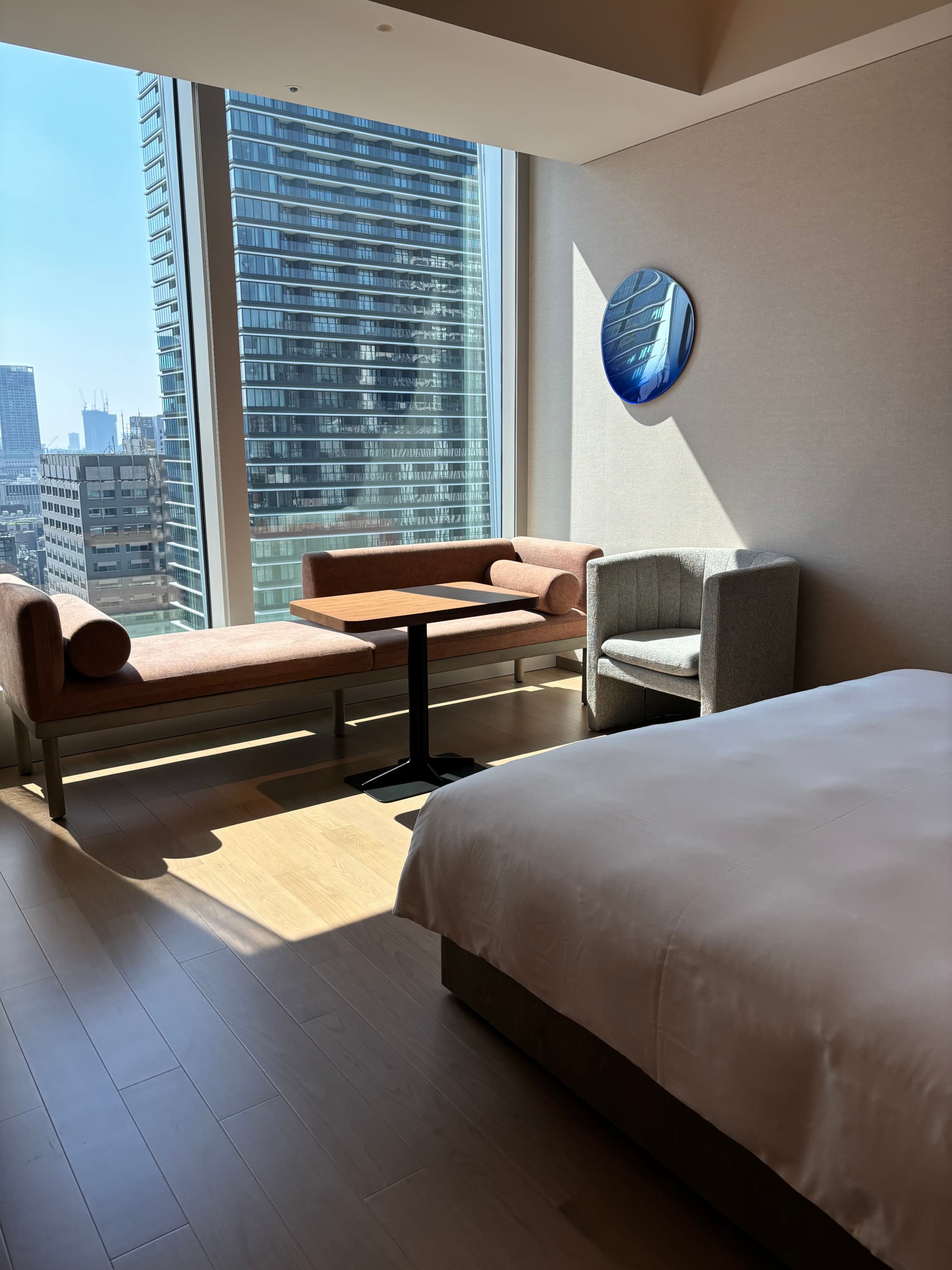 A hotel room with large, floor to ceiling windows looking out onto the city