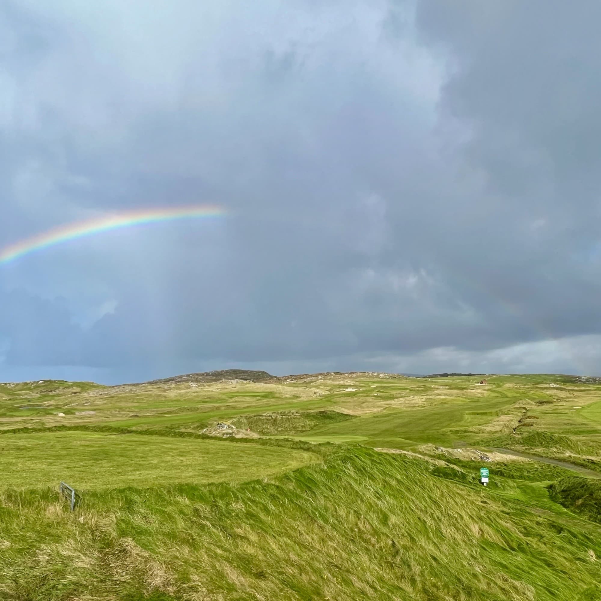 A picturesque landscape featuring a rainbow arching over verdant hills beneath a cloudy sky.