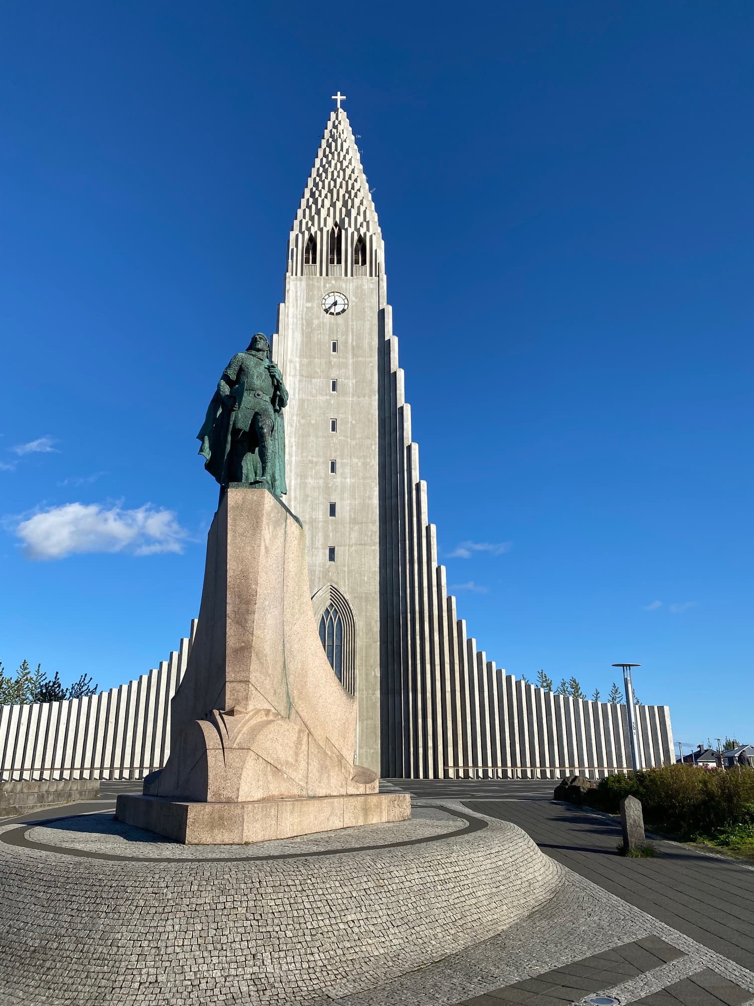 Green statute in front of a tower on a sunny day.