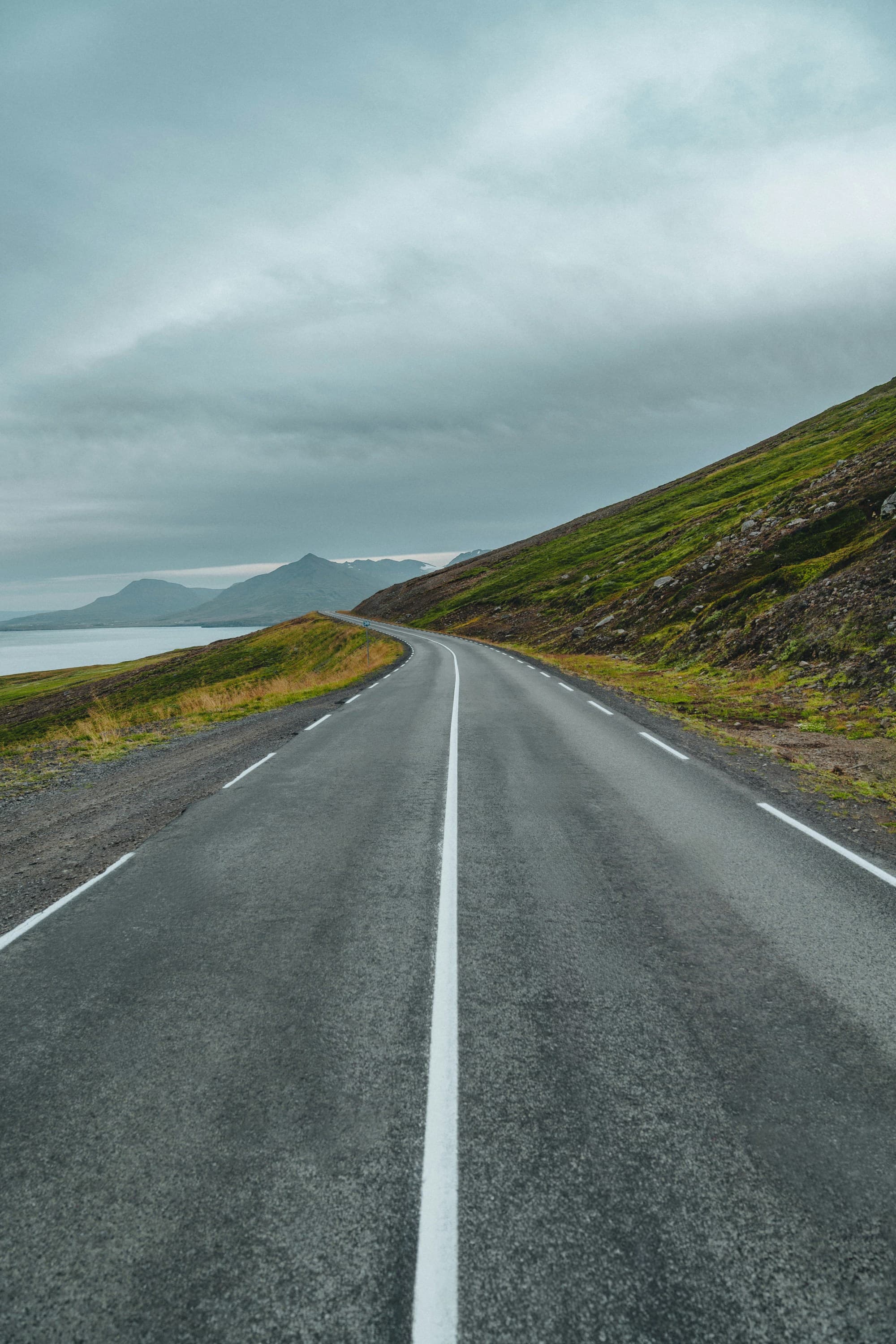 The image depicts a road leading into the distance, flanked by mountains and a cloudy sky, evoking a sense of journey and exploration.