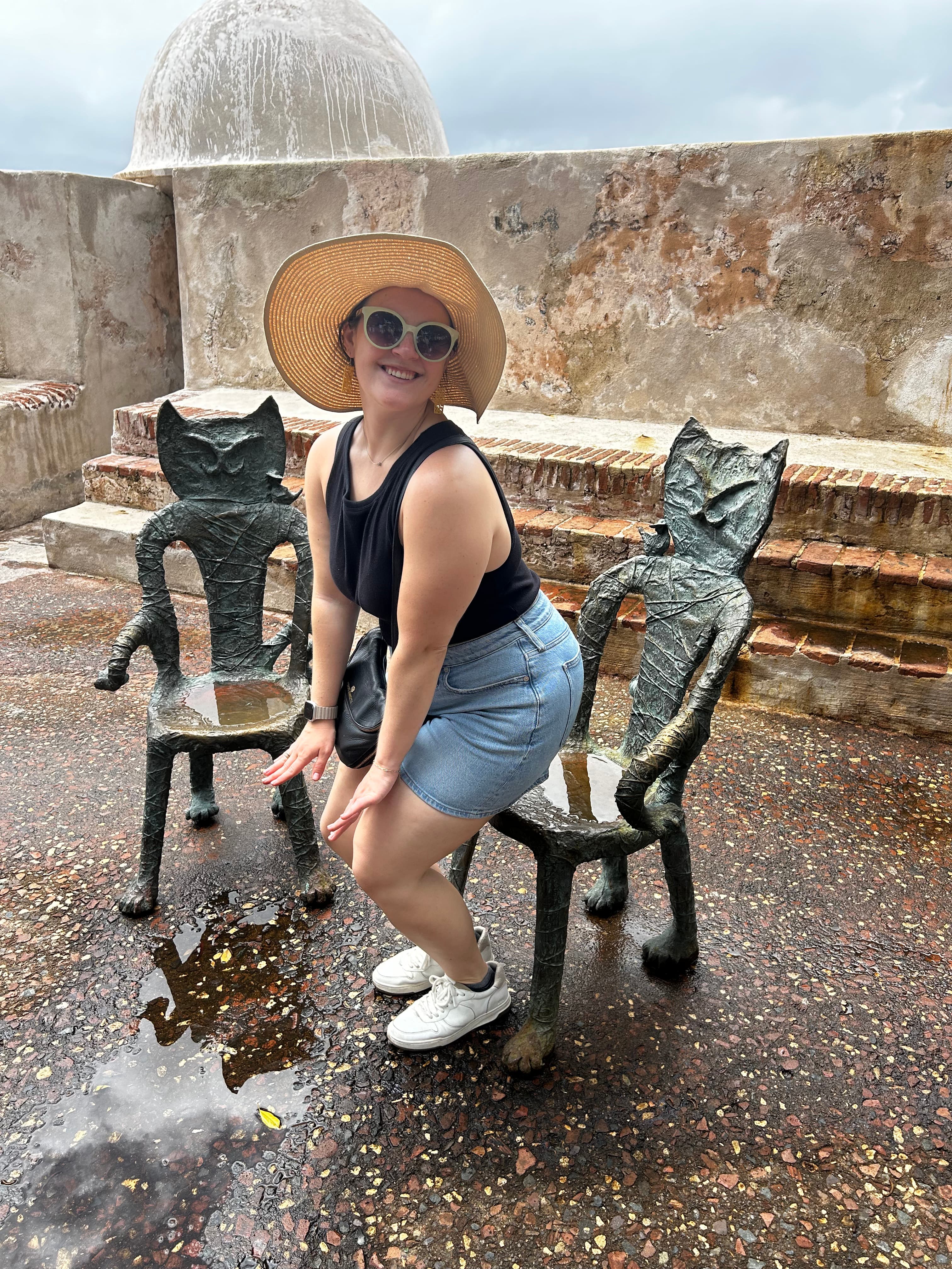 Sculpture cat chairs in San Juan, Puerto Rico with Advisor posing in a hat on a sunny day.