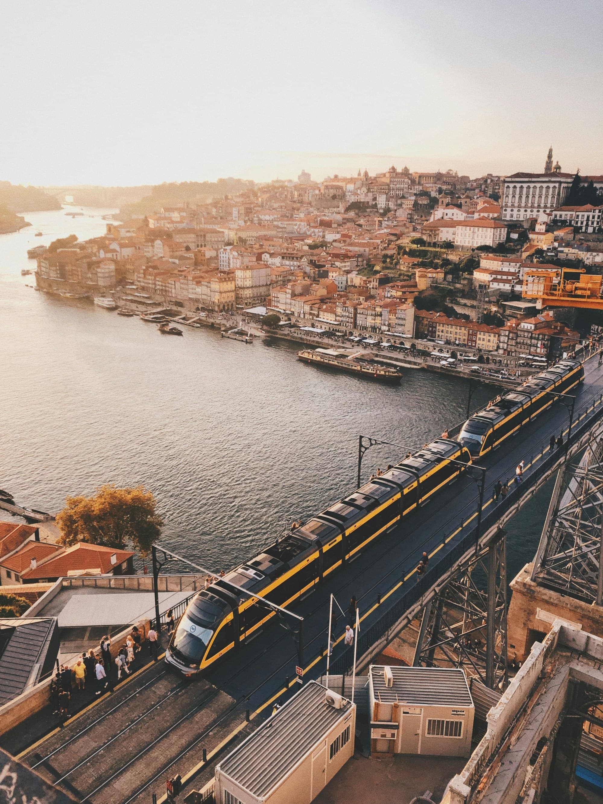 A high-angle view of a cityscape at sunset, featuring a bridge and train over a river.