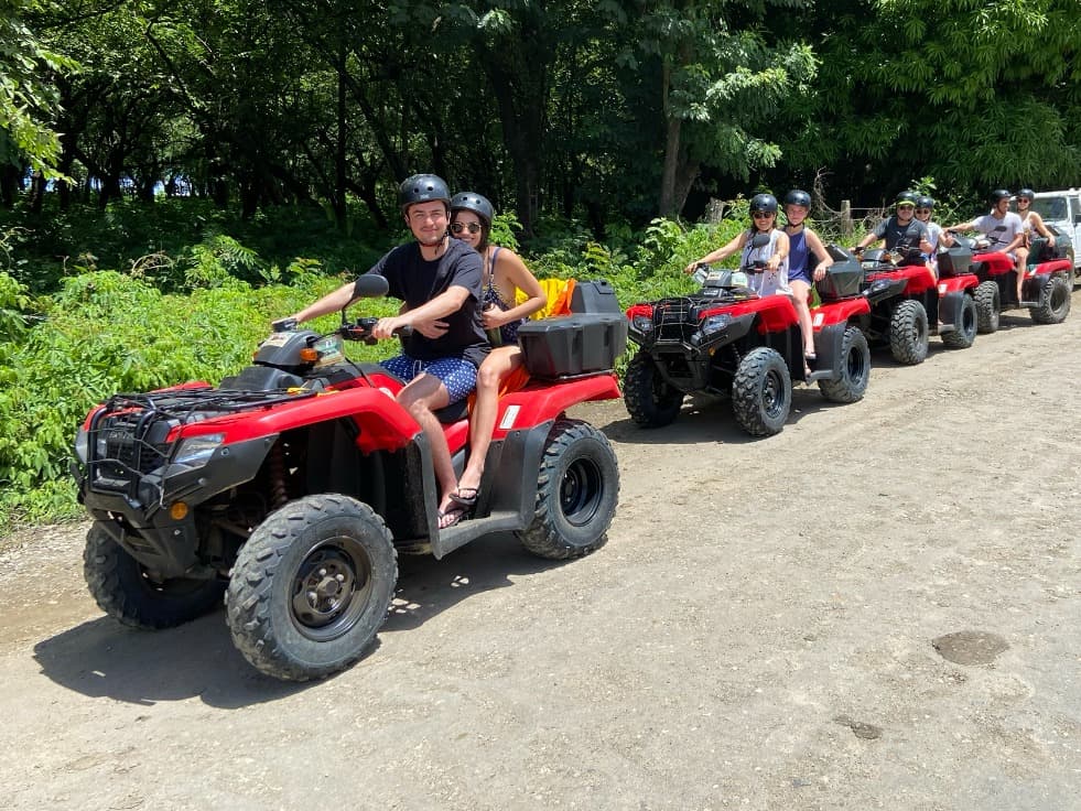 A group of adventurers on ATVs, ready for an off-road journey amidst a forested trail on a sunny day.