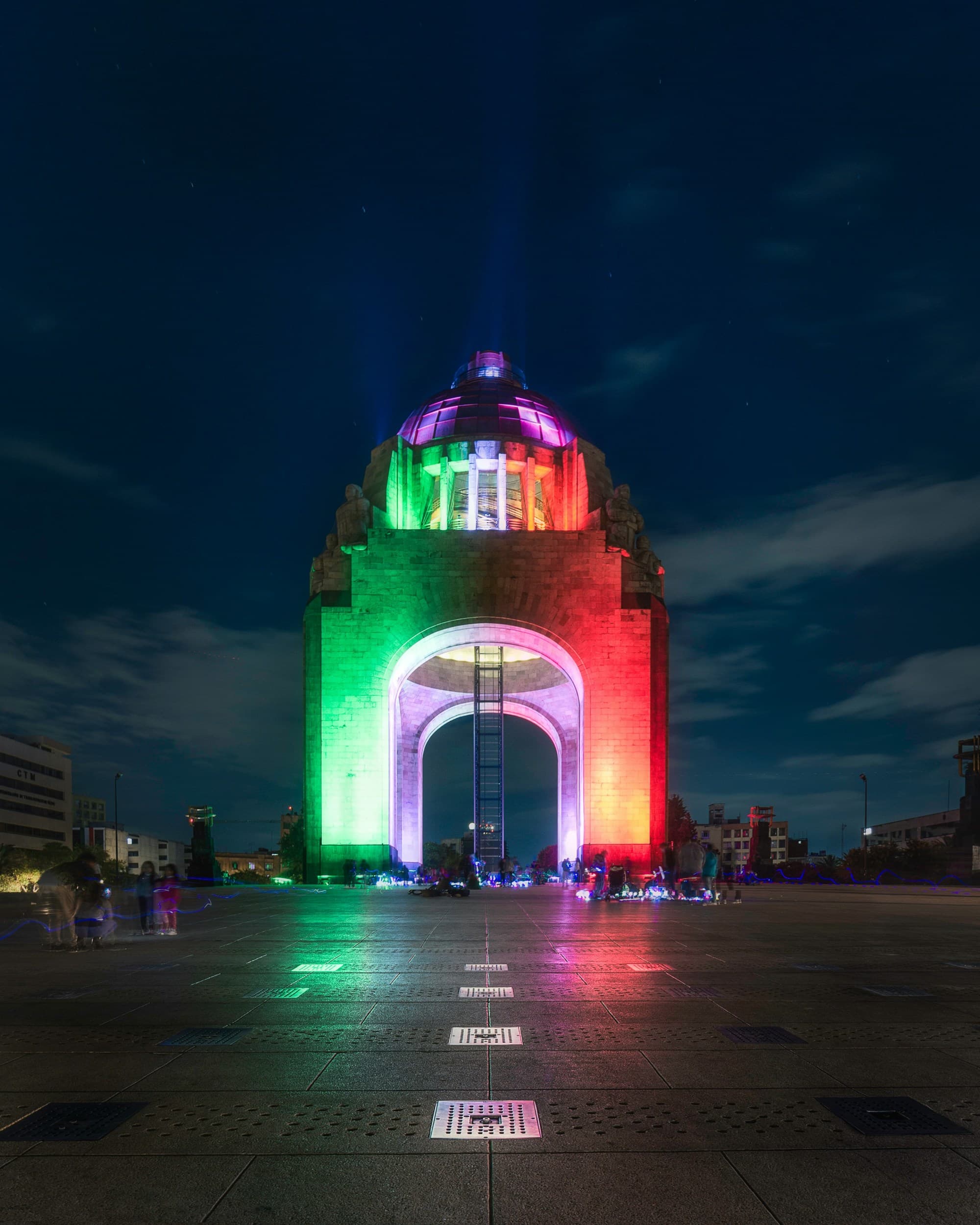 A monument at night lit up in the colors of the Mexican flag.