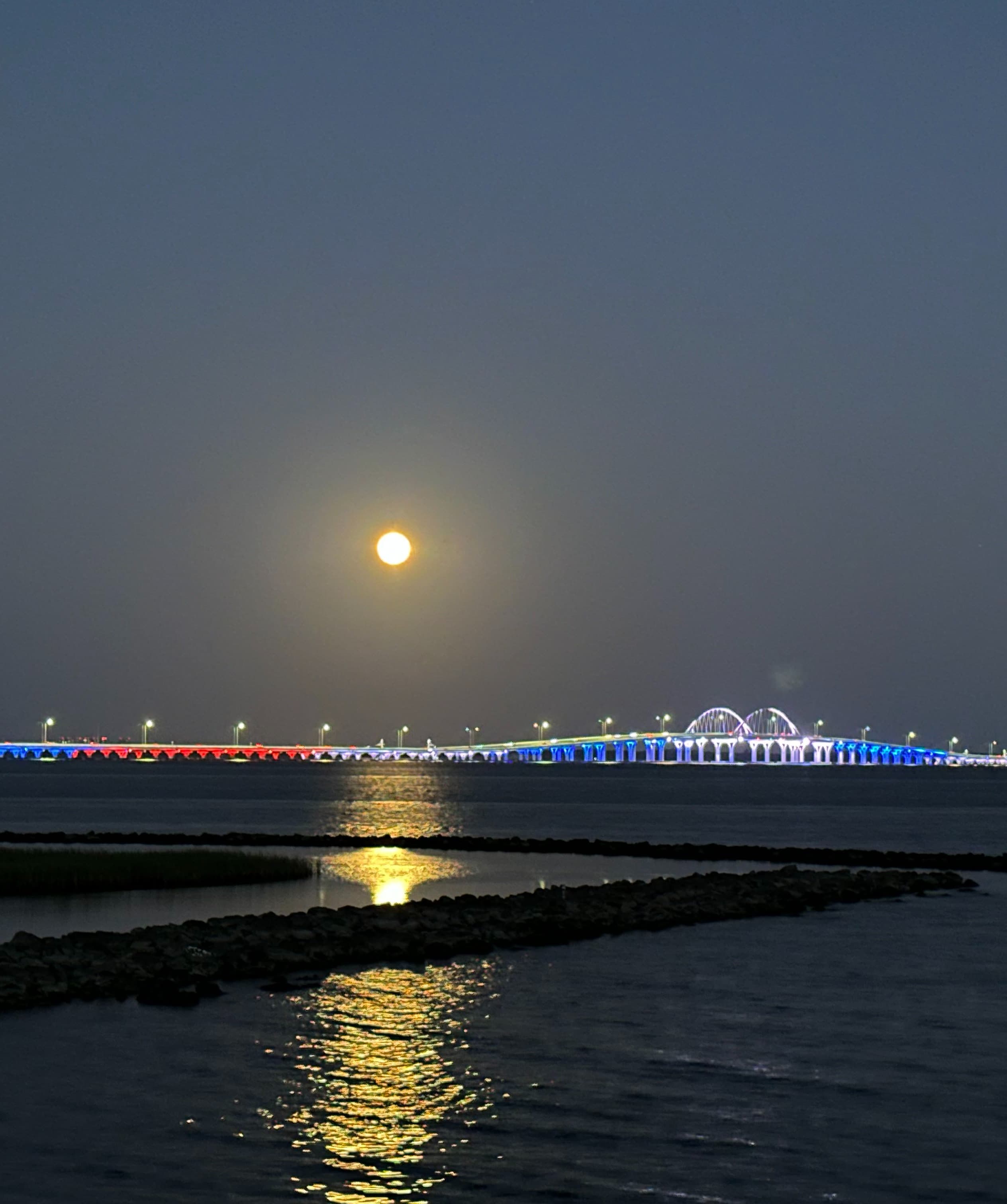Pensacola's Three Mile Bridge lit up in red white and blue with a full moon overhead.