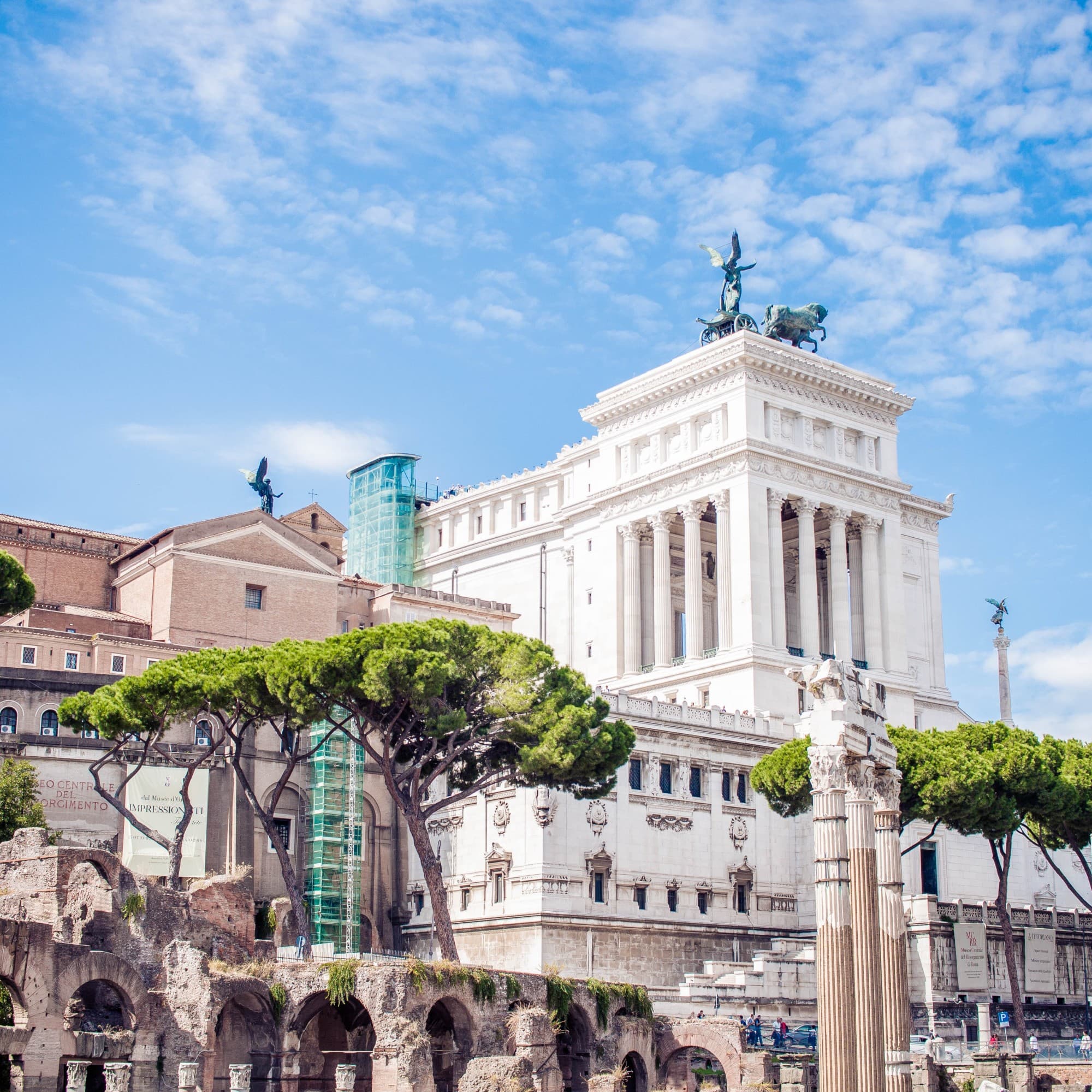 A view of historic buildings reaching toward the sky on a clear day dotted with clouds.