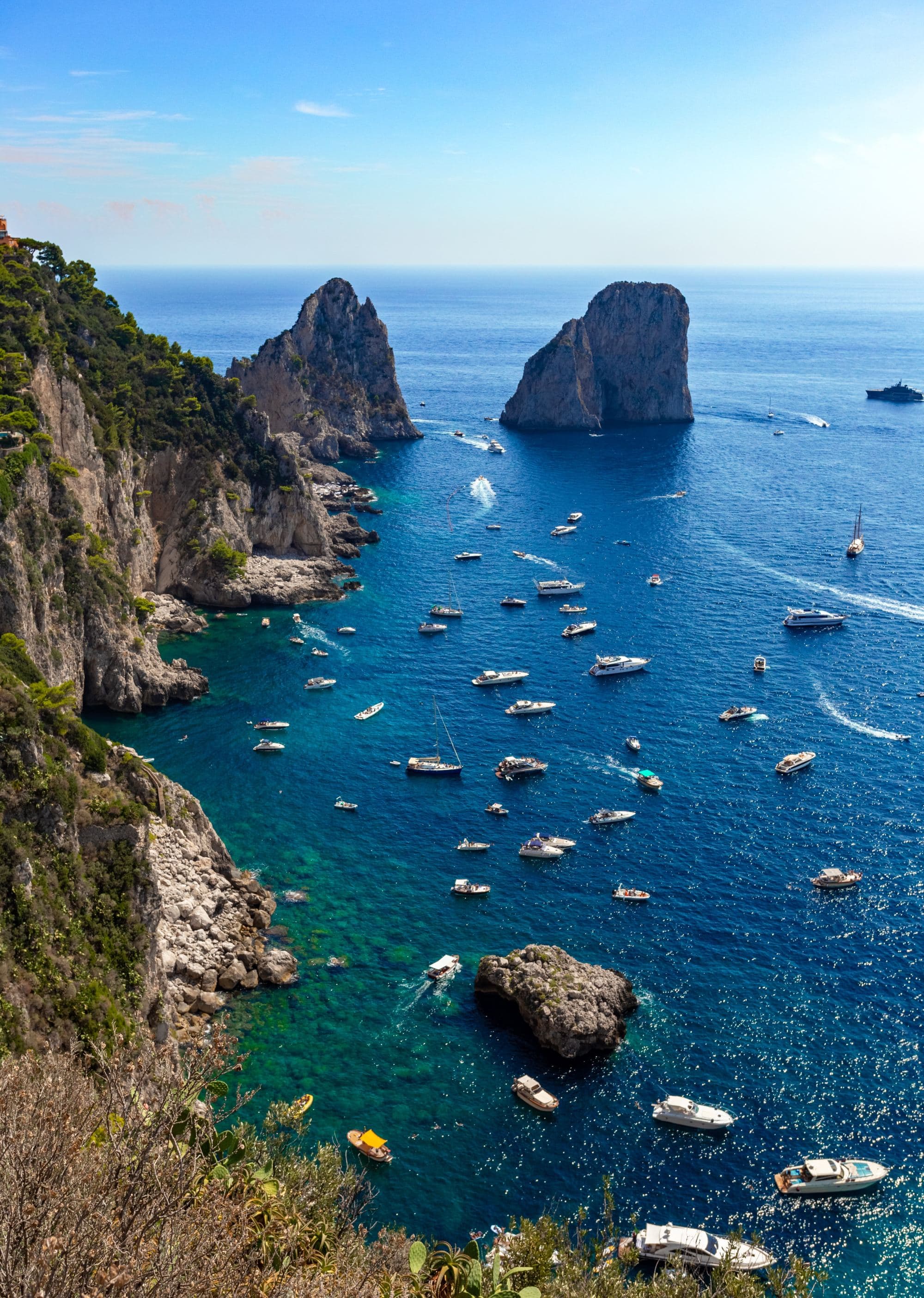 blue waters off an island with rock formations in the water and dotted with boats
